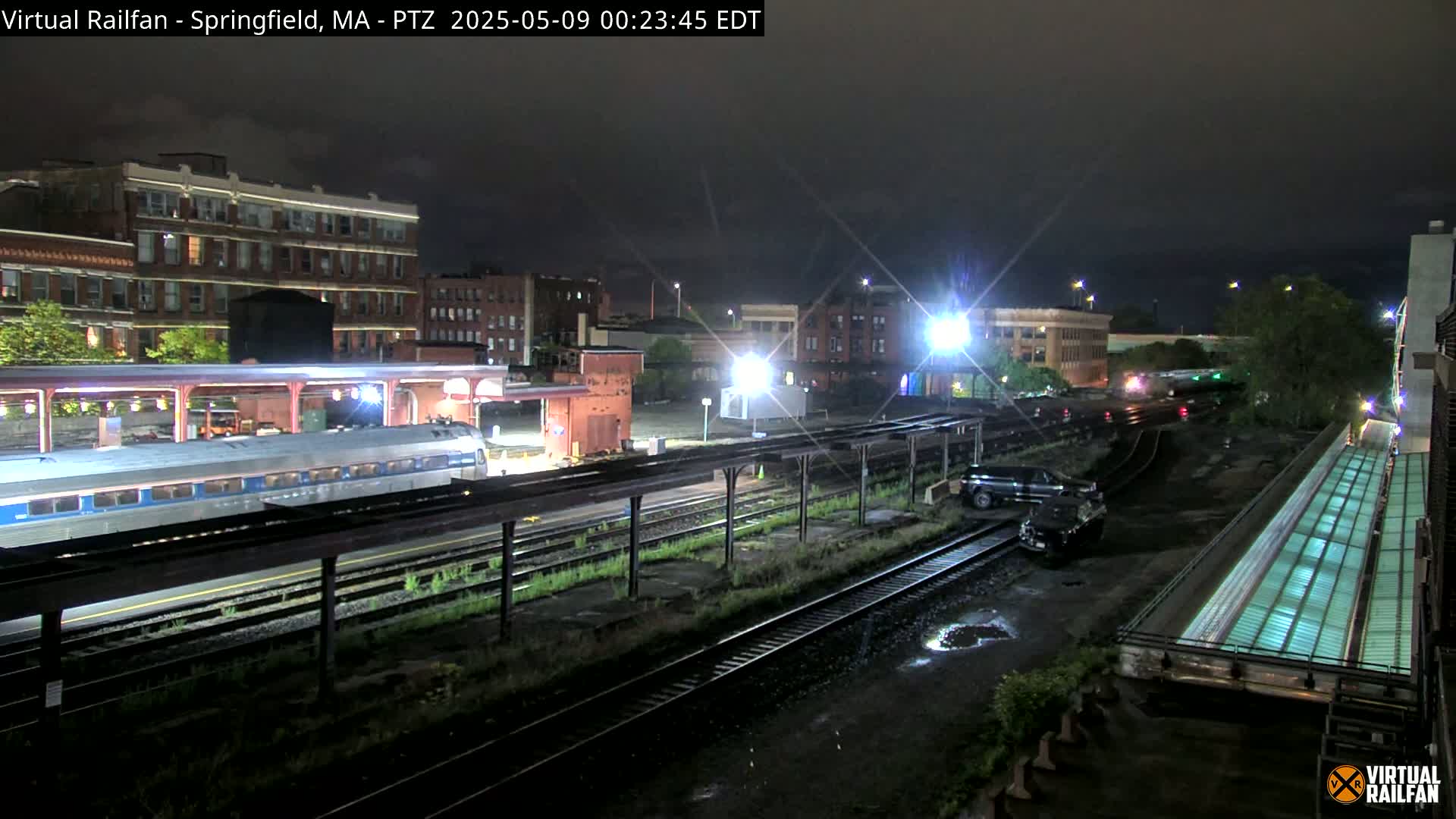 A nighttime view of a train at a station, under a dark sky with some rain.