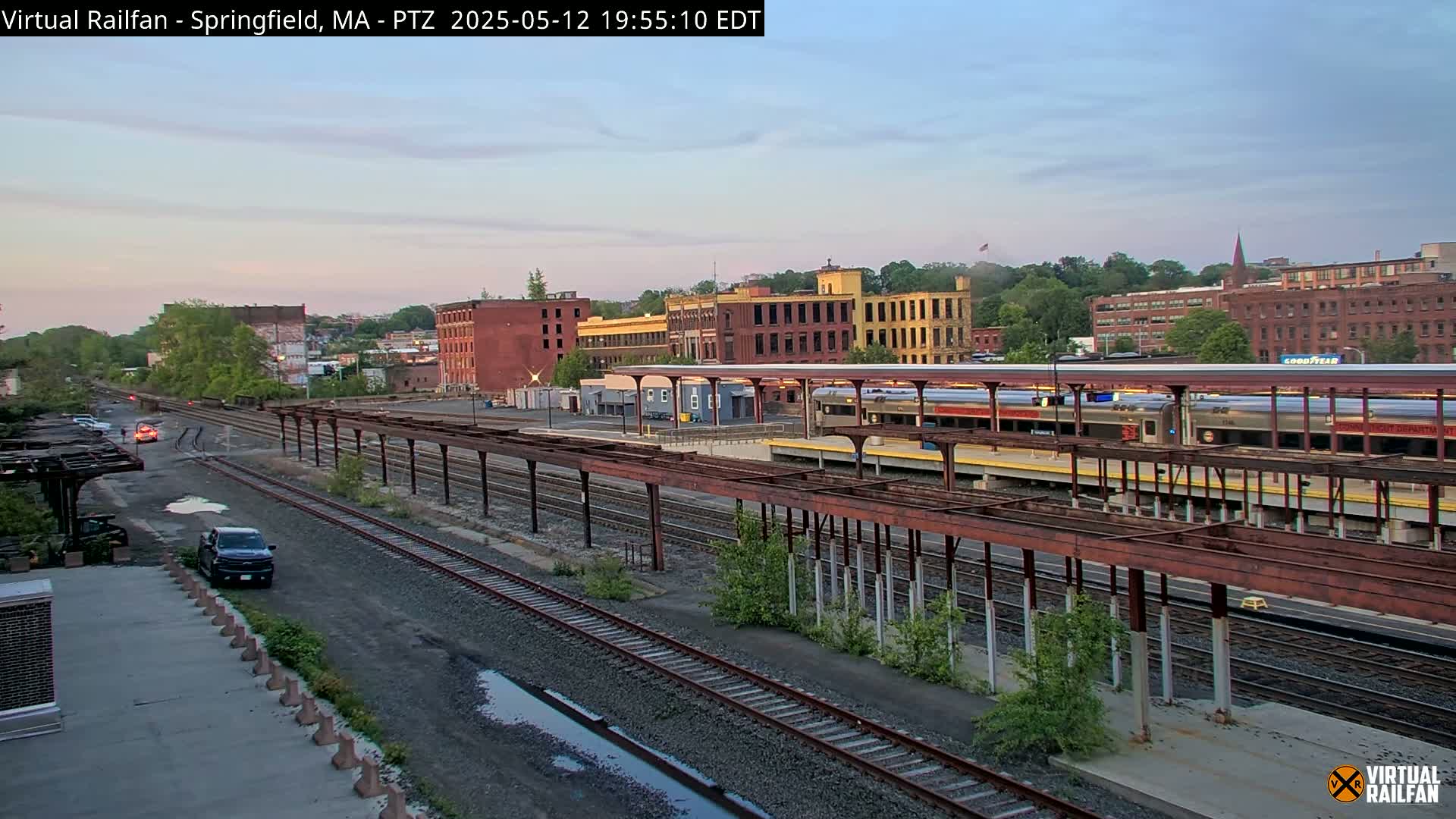 A train sits at a station next to several multi-story brick buildings under a twilight sky.