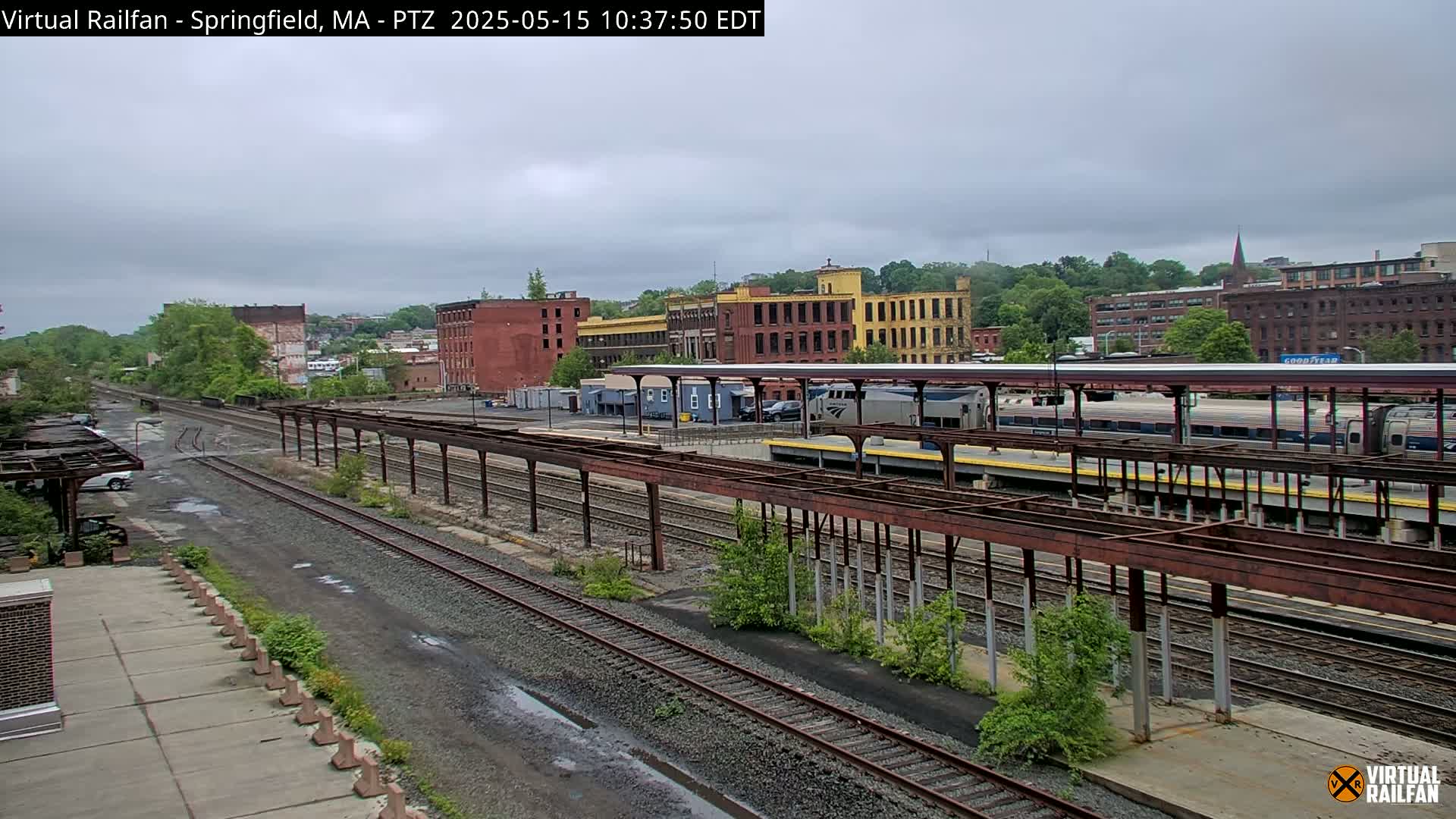 A train sits at a station amongst several sets of train tracks under an overcast sky.