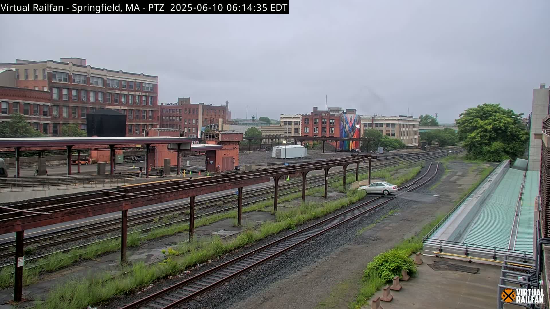 A train station with multiple tracks and several brick buildings in the background on an overcast day.