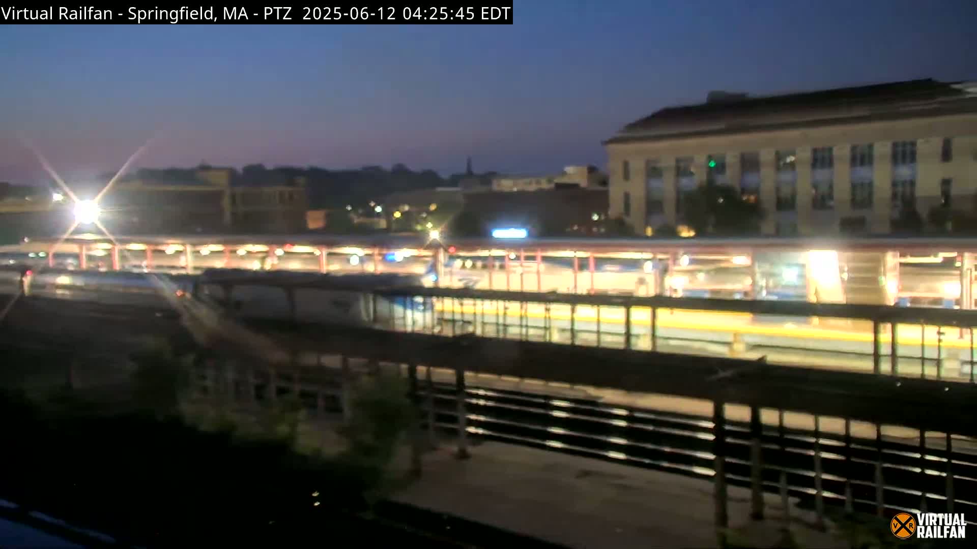 A nighttime view of a train station with a train at the platform under a twilight sky.