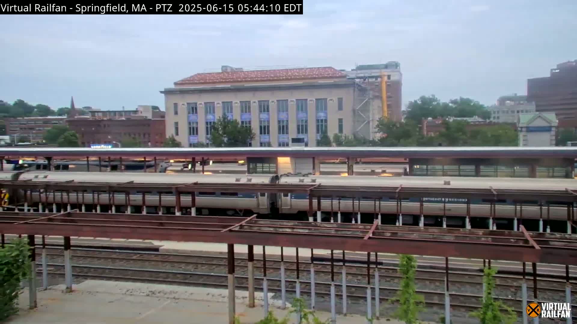 A passenger train sits at a station platform under an overcast sky.