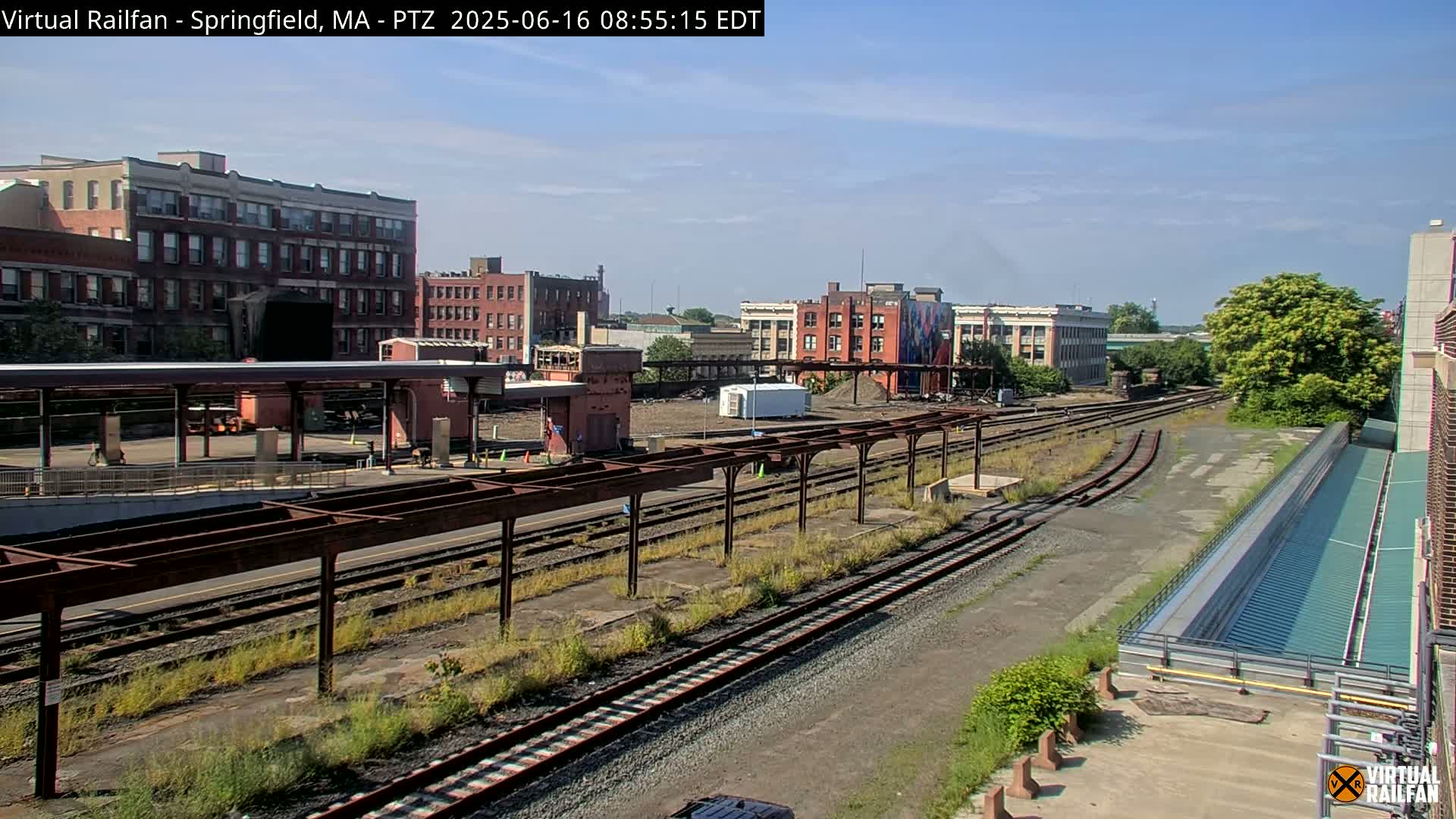 A train station with several train tracks and surrounding buildings under a partly cloudy sky.