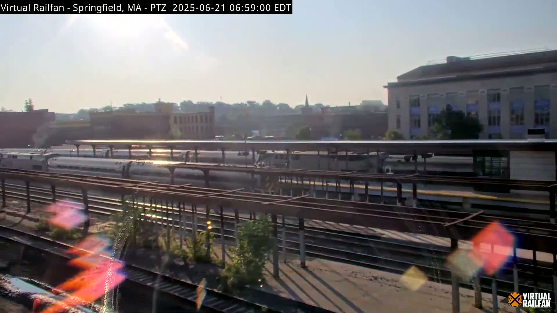 Several passenger trains are parked at a station platform on a sunny morning.