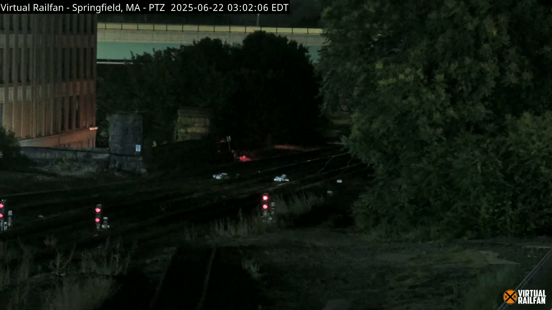 A nighttime view of railroad tracks next to a building and trees under dark conditions.