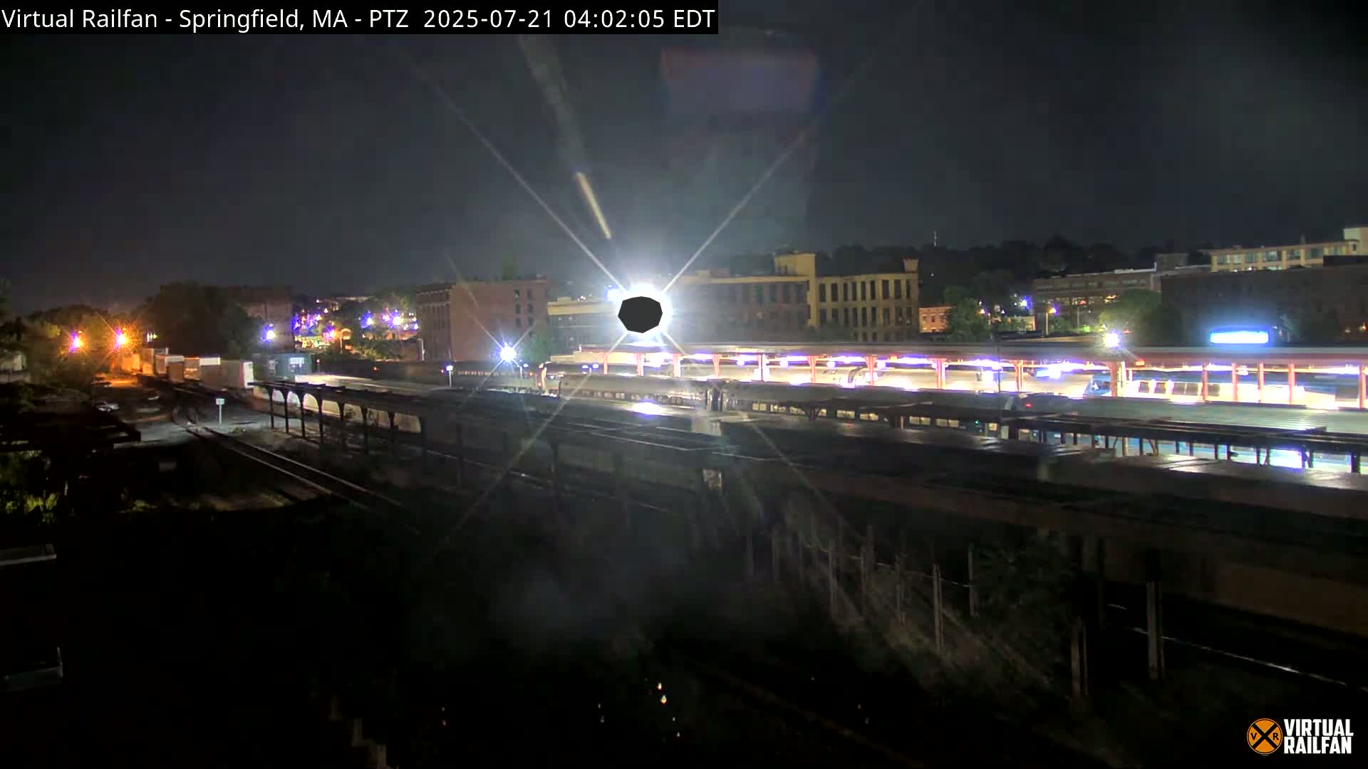 A nighttime view of a train station with several passenger cars parked under a covered platform, illuminated by artificial lights.