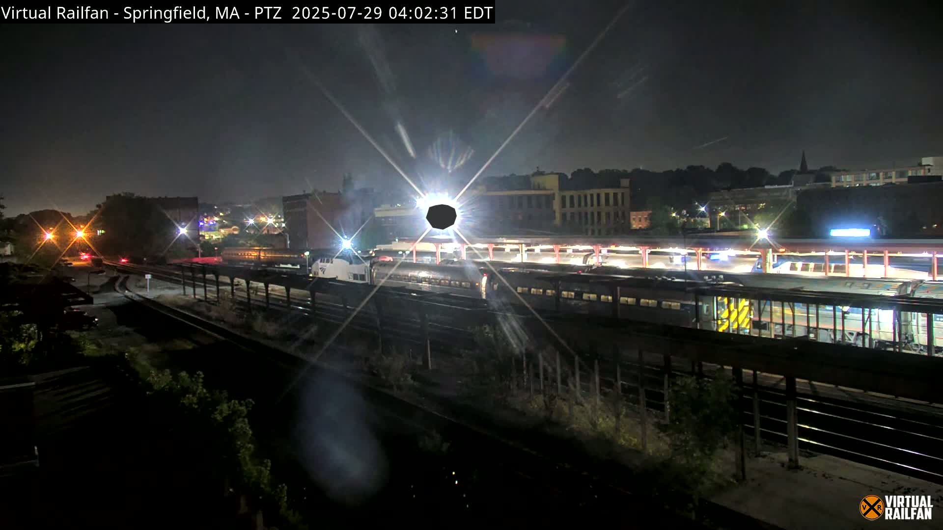 A nighttime view of a train station with several passenger trains at the platform under a clear sky.