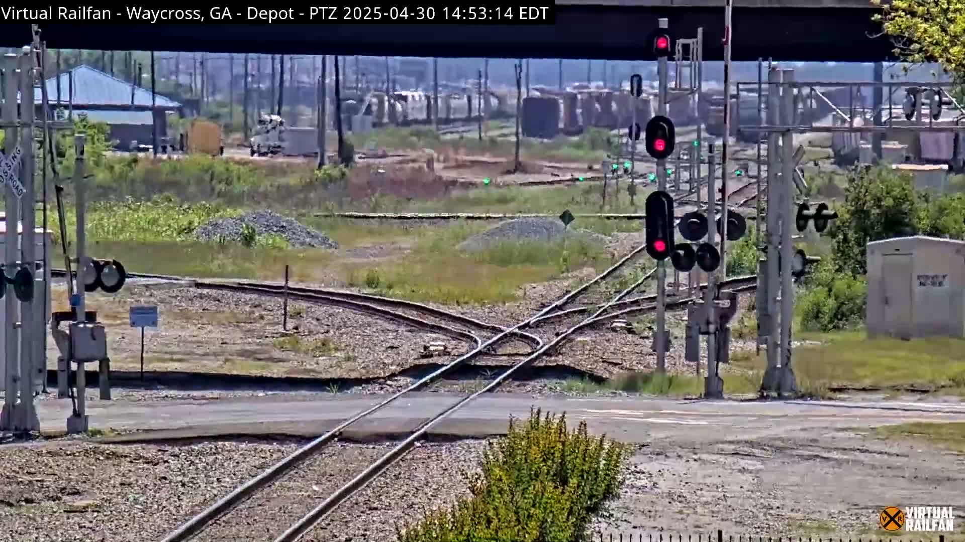 A railroad crossing with several sets of tracks and signal lights showing red under a mostly clear sky.