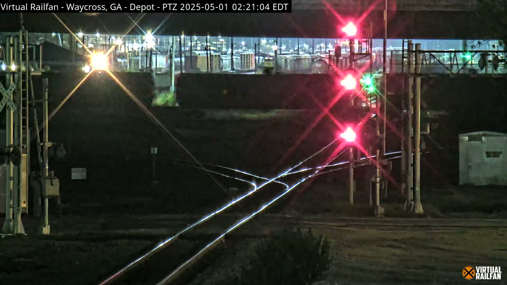 At night, a railroad crossing shows red signal lights illuminating intersecting train tracks.