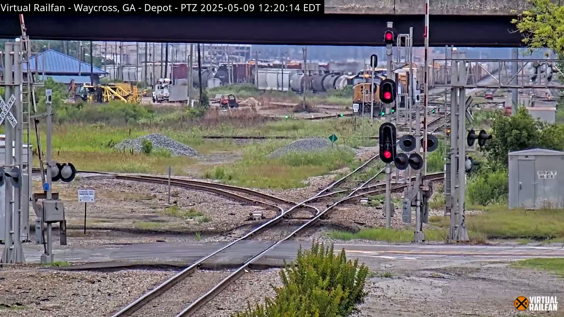 A railway intersection with a yellow locomotive and several railcars in the background under an overcast sky.