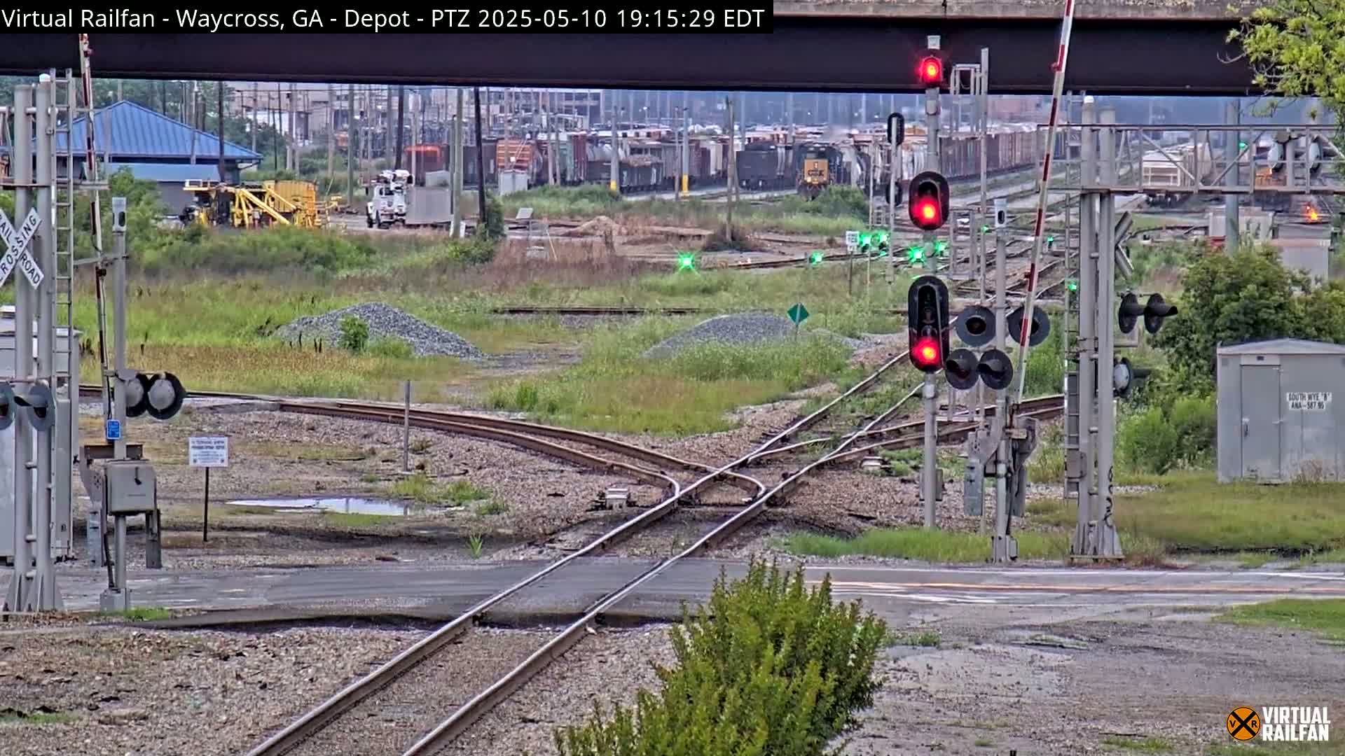 A railroad crossing with several sets of train tracks converging, featuring railroad signals, and a mostly overcast sky.