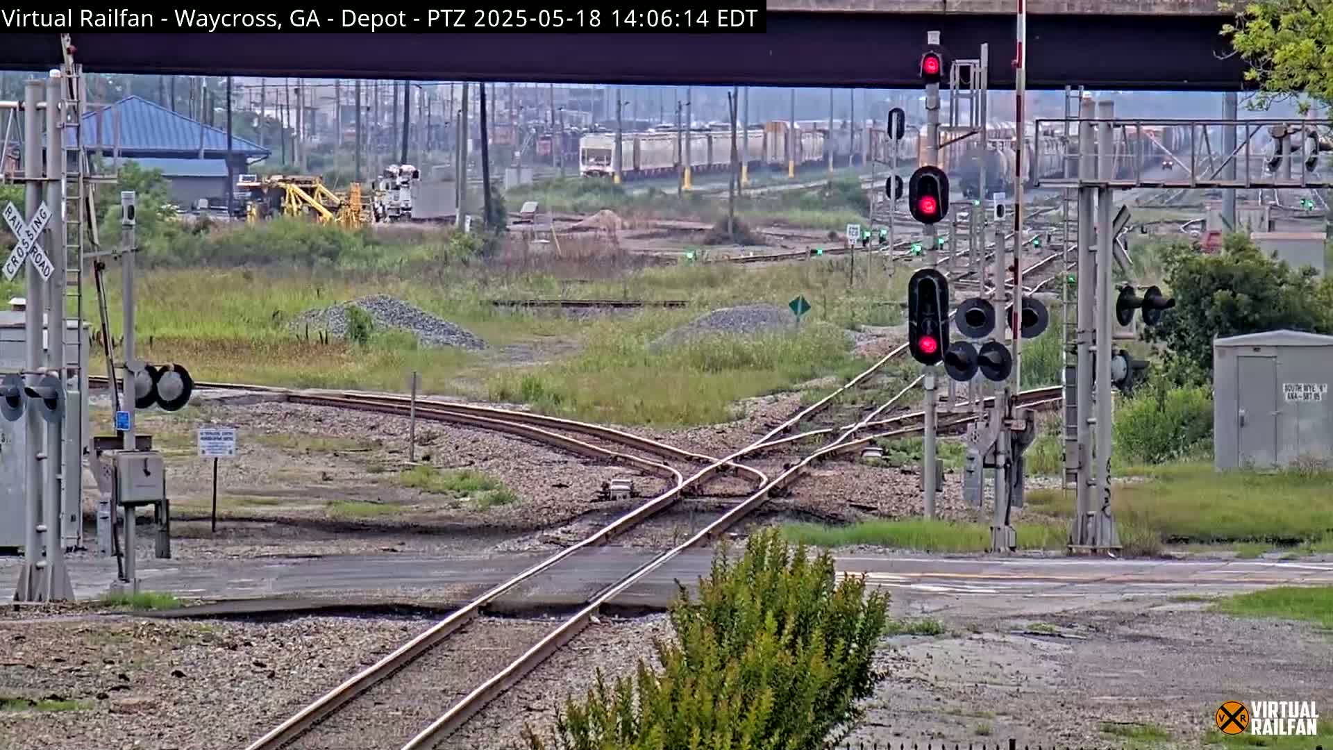 A railroad crossing with several sets of tracks converging, featuring a red traffic signal, under an overcast sky.