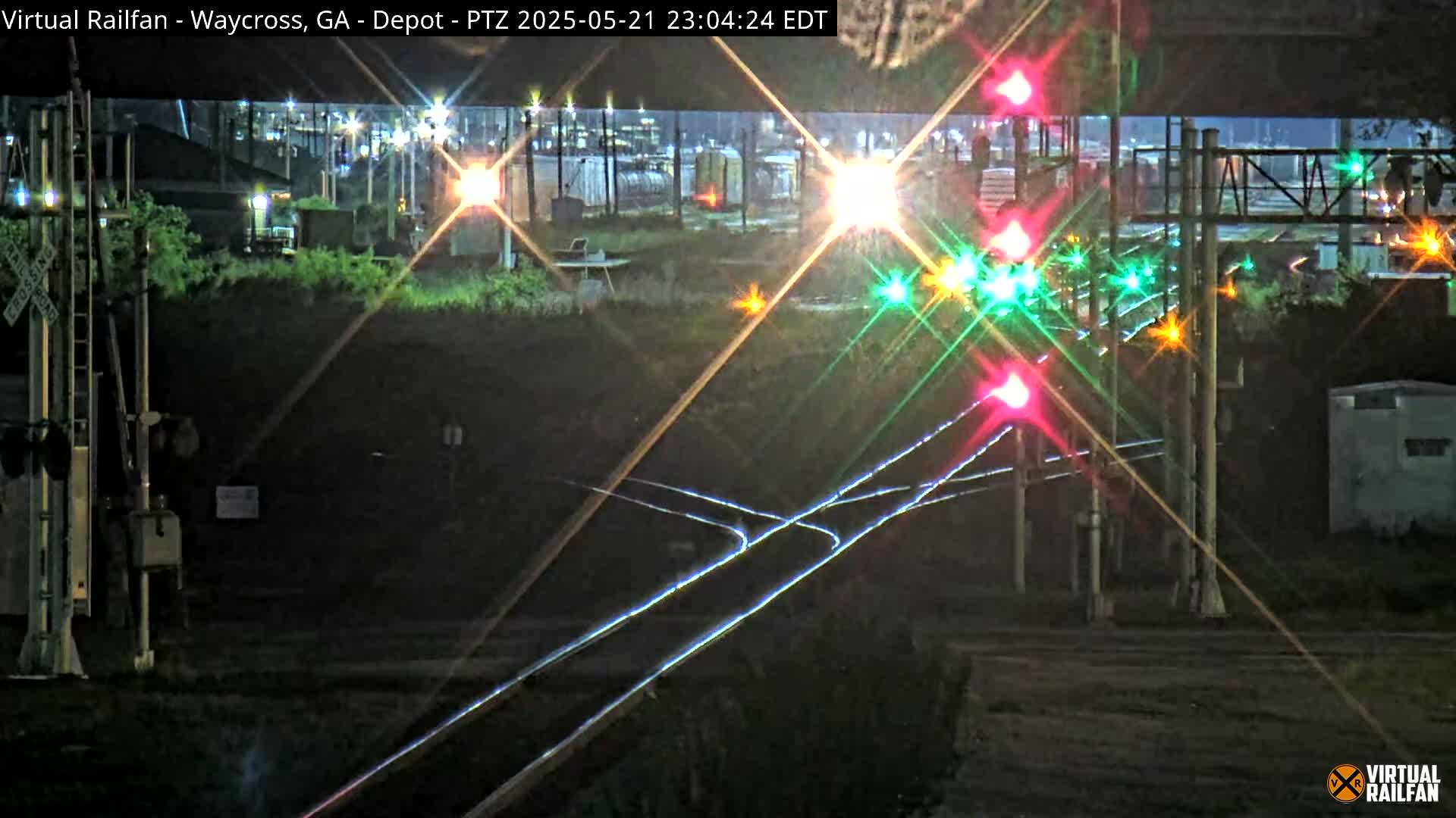 A nighttime view of a railroad crossing with illuminated signals and train tracks, under dark, clear skies.