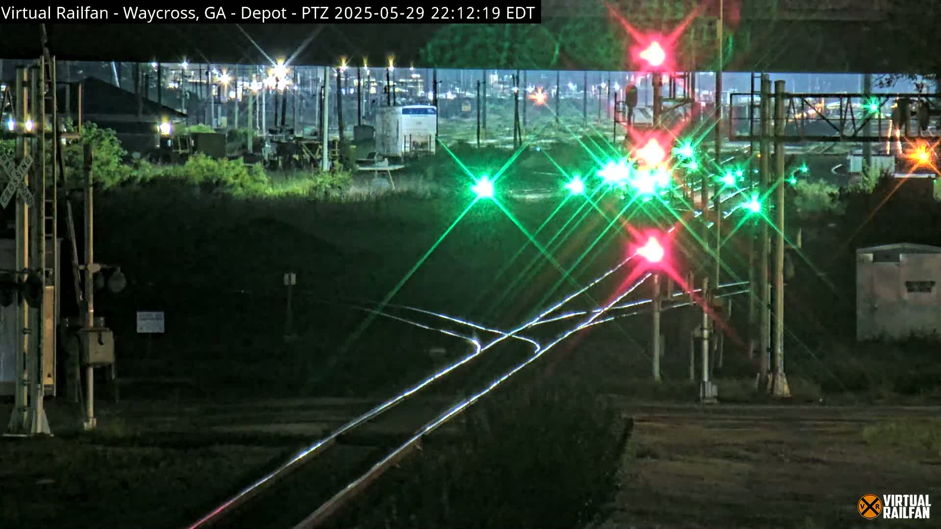 At night, railroad tracks intersect with a road, illuminated by green and red railroad crossing lights.
