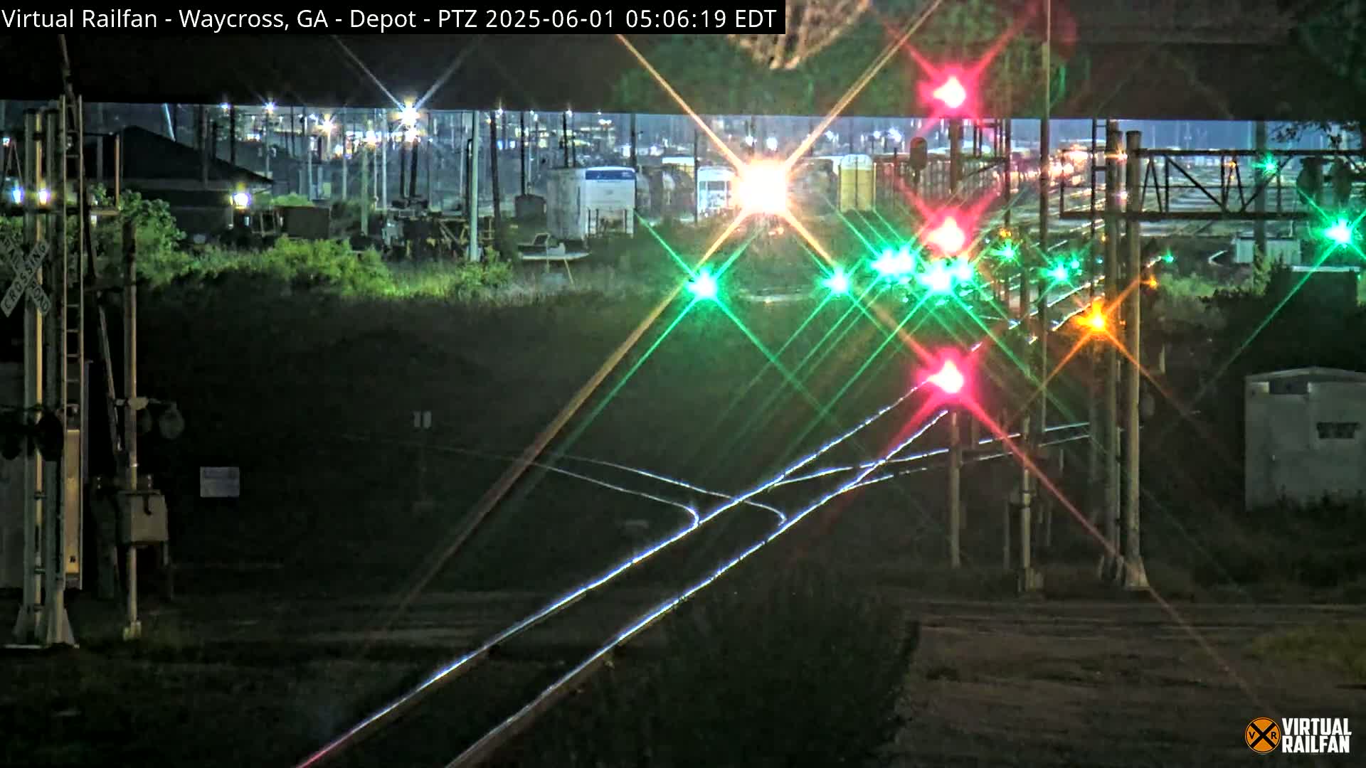 At night, a train passes by a railroad crossing with illuminated signals, under a clear sky.