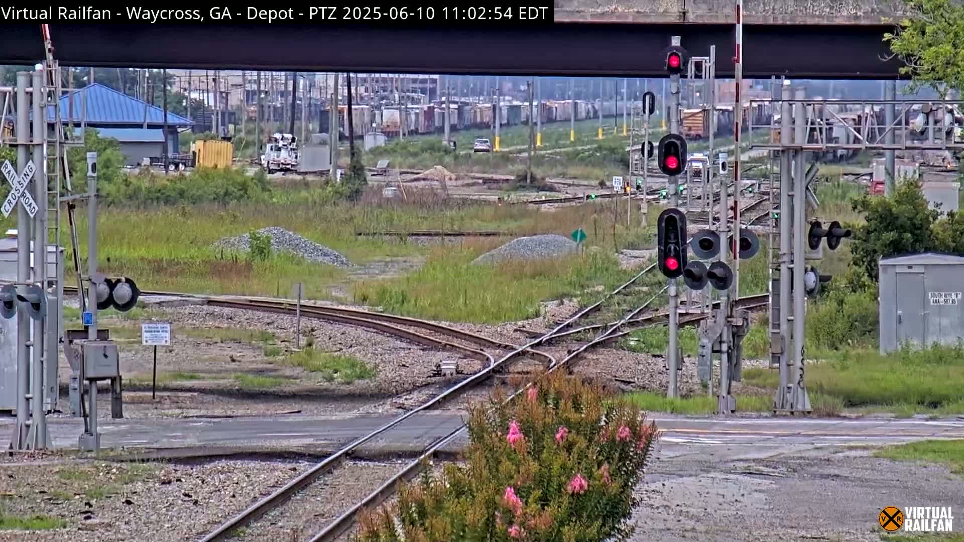 A railroad crossing with several sets of red train signals is shown, with a railway track splitting into two directions, under an overcast sky.