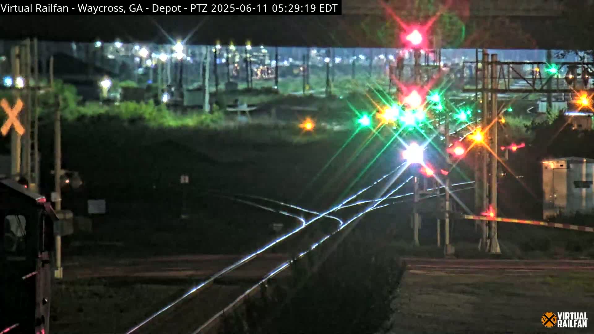 At night, a train sits at a rail yard with a complex network of tracks and illuminated signals.