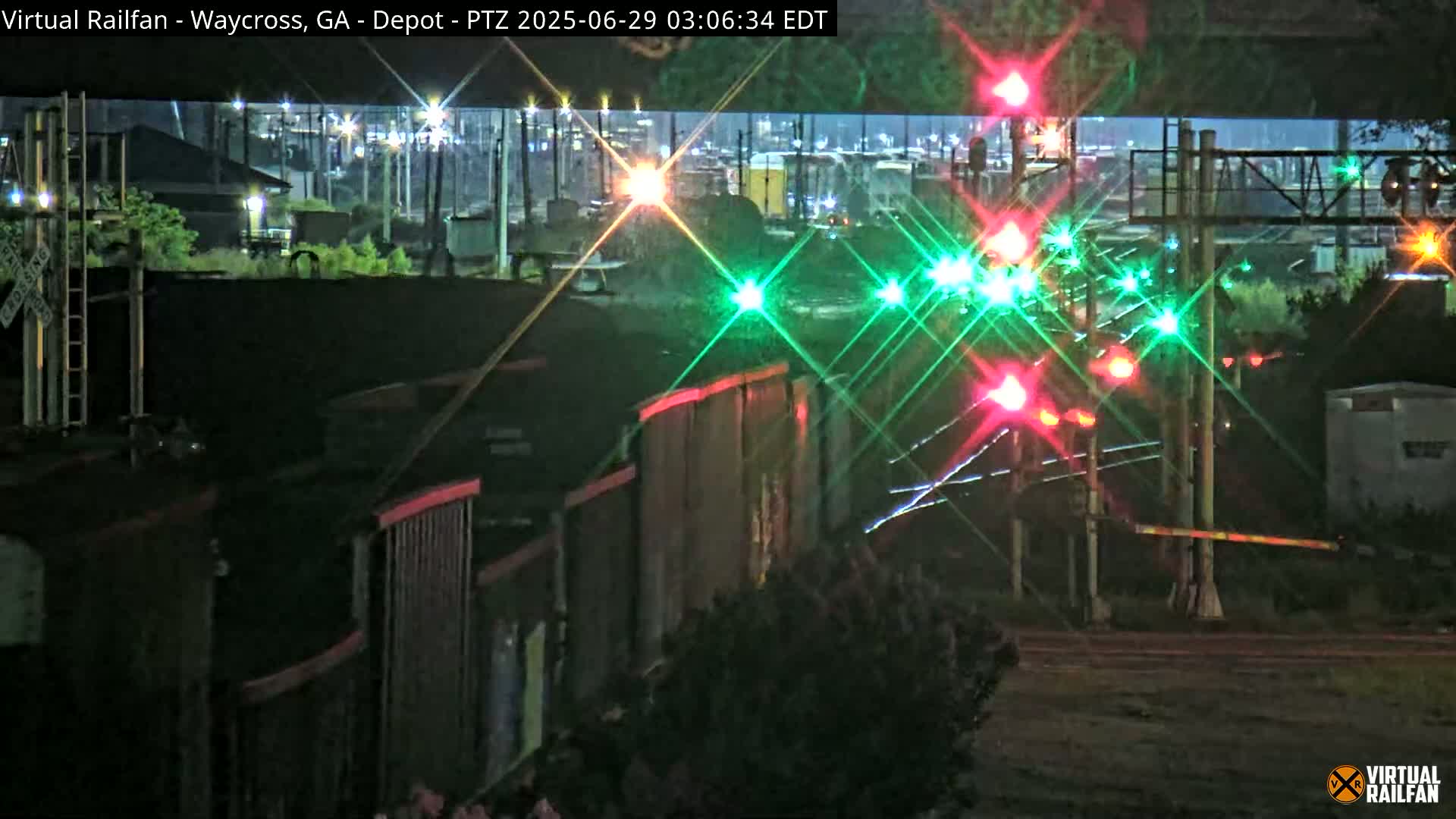 At night, a train passes by a rail crossing with illuminated red and green lights, under a clear sky.