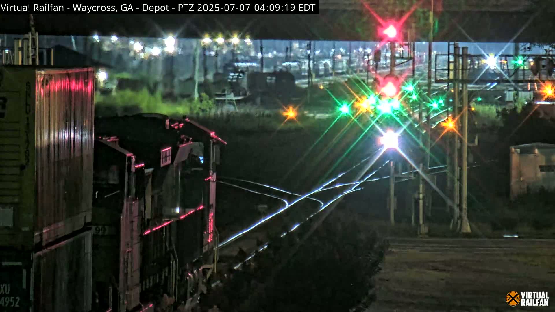 At night, a train locomotive approaches a railroad crossing with illuminated signals.