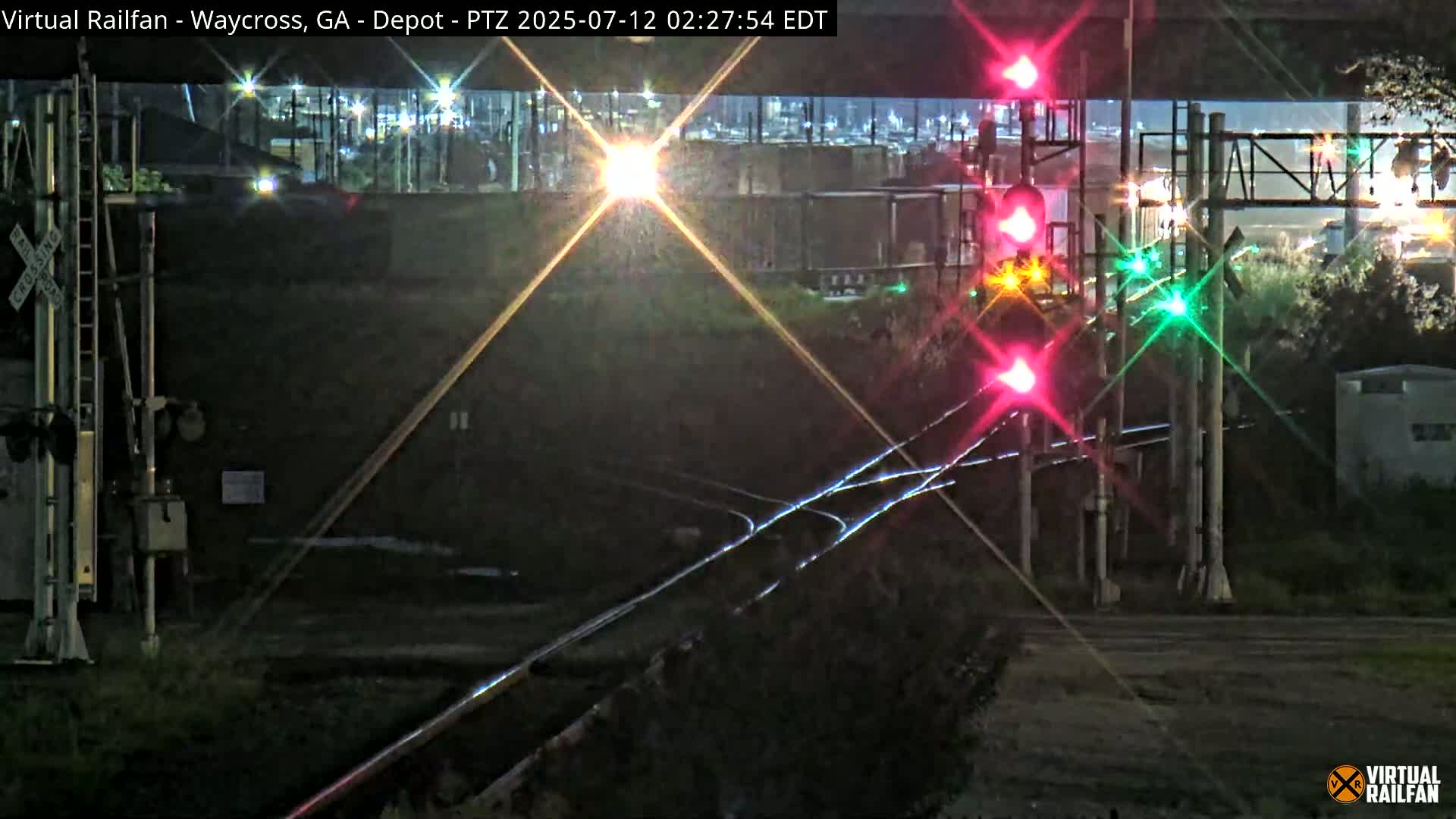 At night, a train locomotive approaches a railroad crossing with illuminated signals.