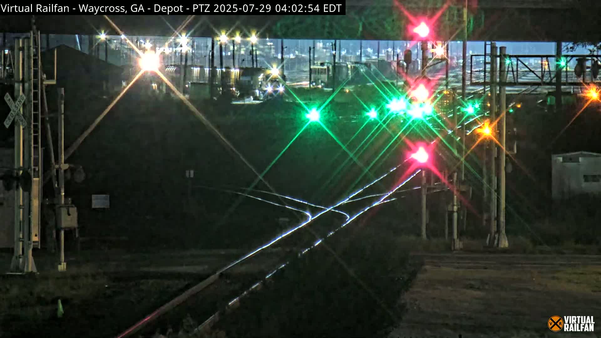 A nighttime view of a railroad crossing with multiple signal lights illuminated, some showing red and others green, under a dark sky.