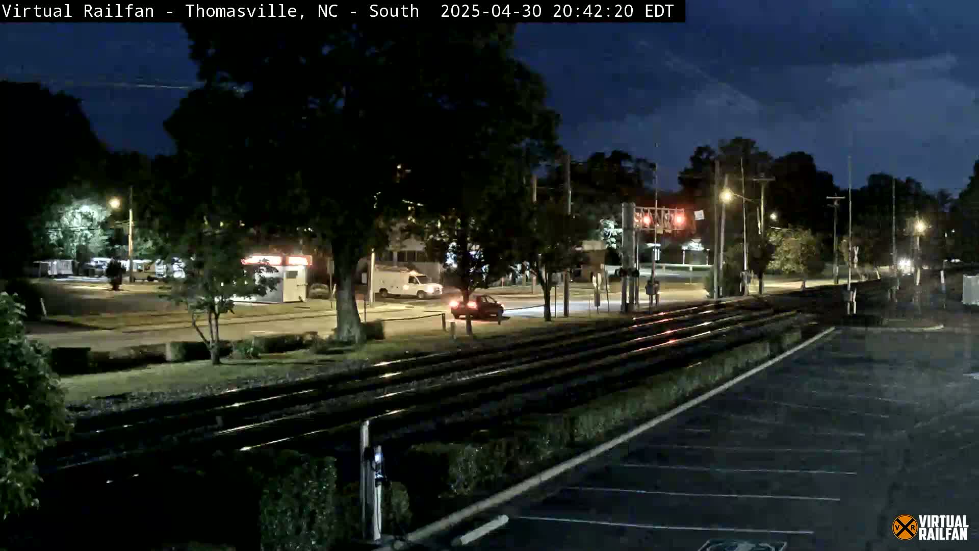 A nighttime view of a street intersection near railroad tracks, with a few cars visible under a clear, dark sky.
