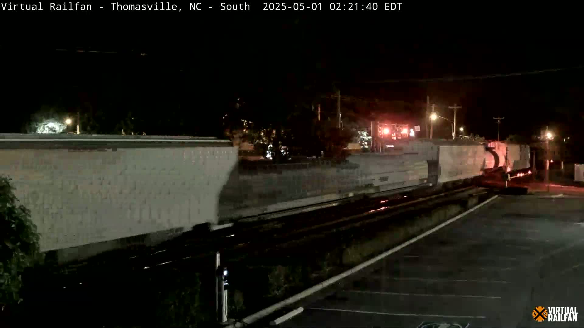 A long freight train passes at night on a railroad track next to a dark parking lot.