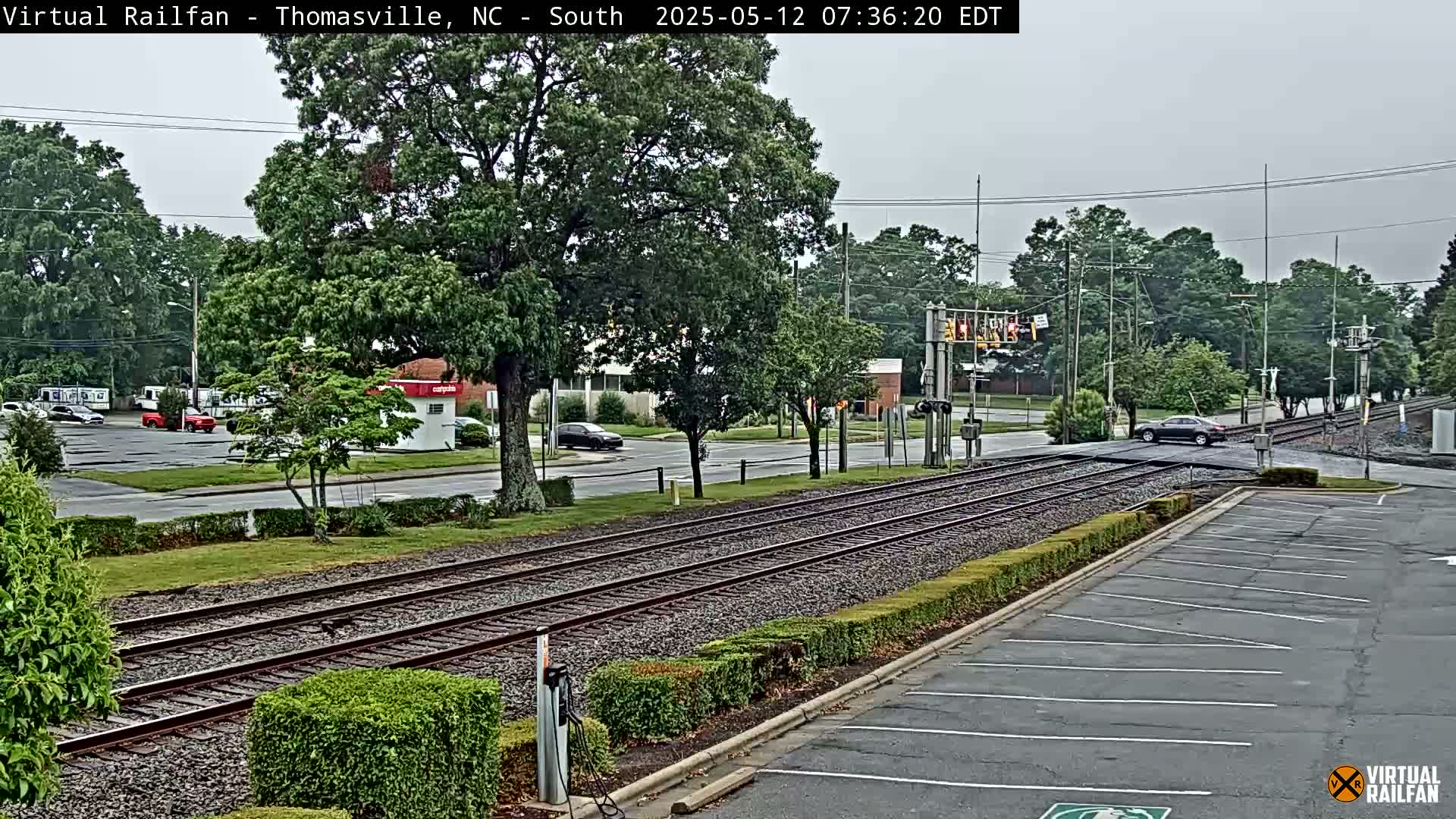 A view of railroad tracks intersecting a road in a tree-lined area under an overcast sky.