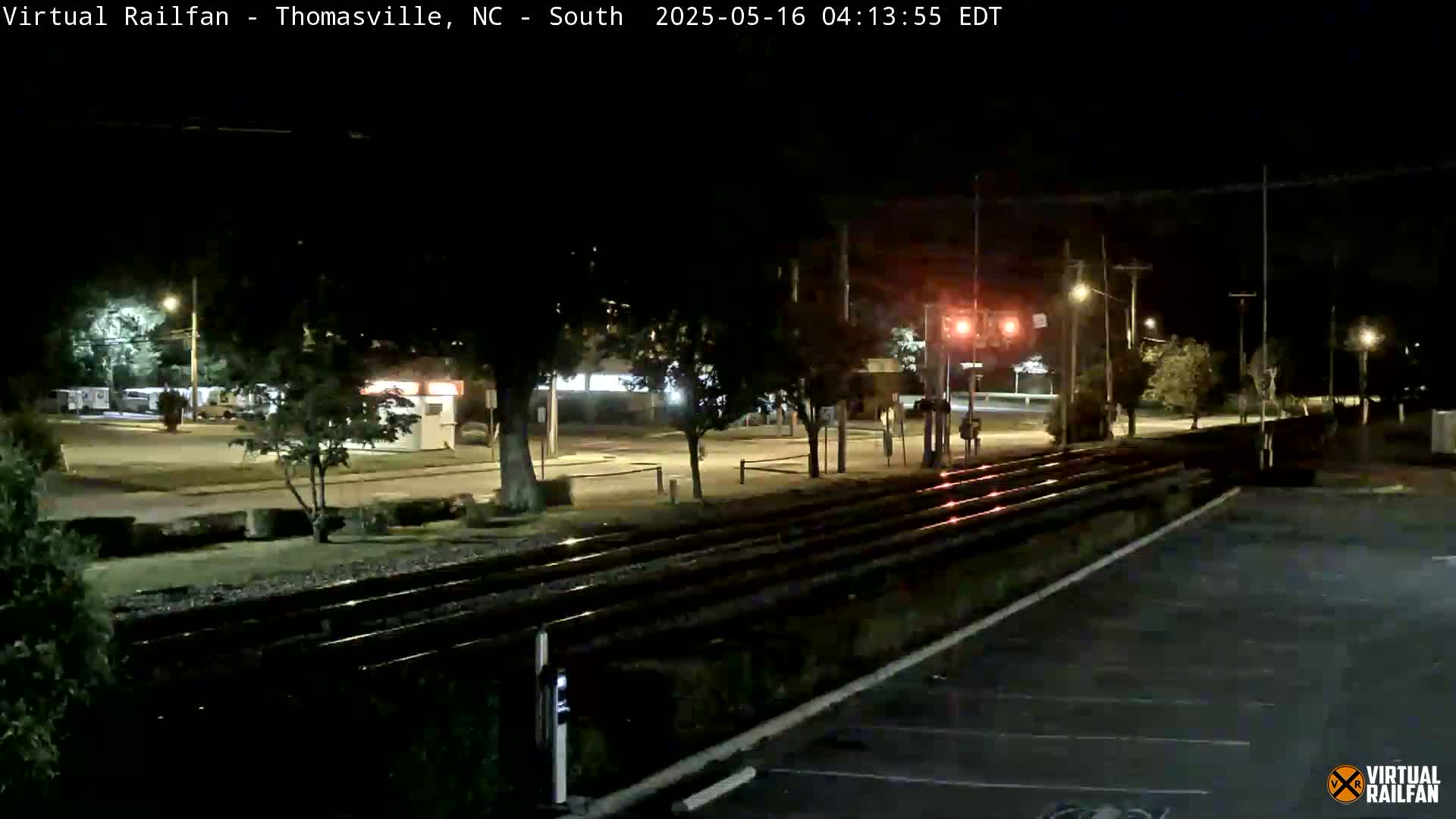 A nighttime view of railroad tracks intersecting a road, with streetlights illuminating the surrounding area.