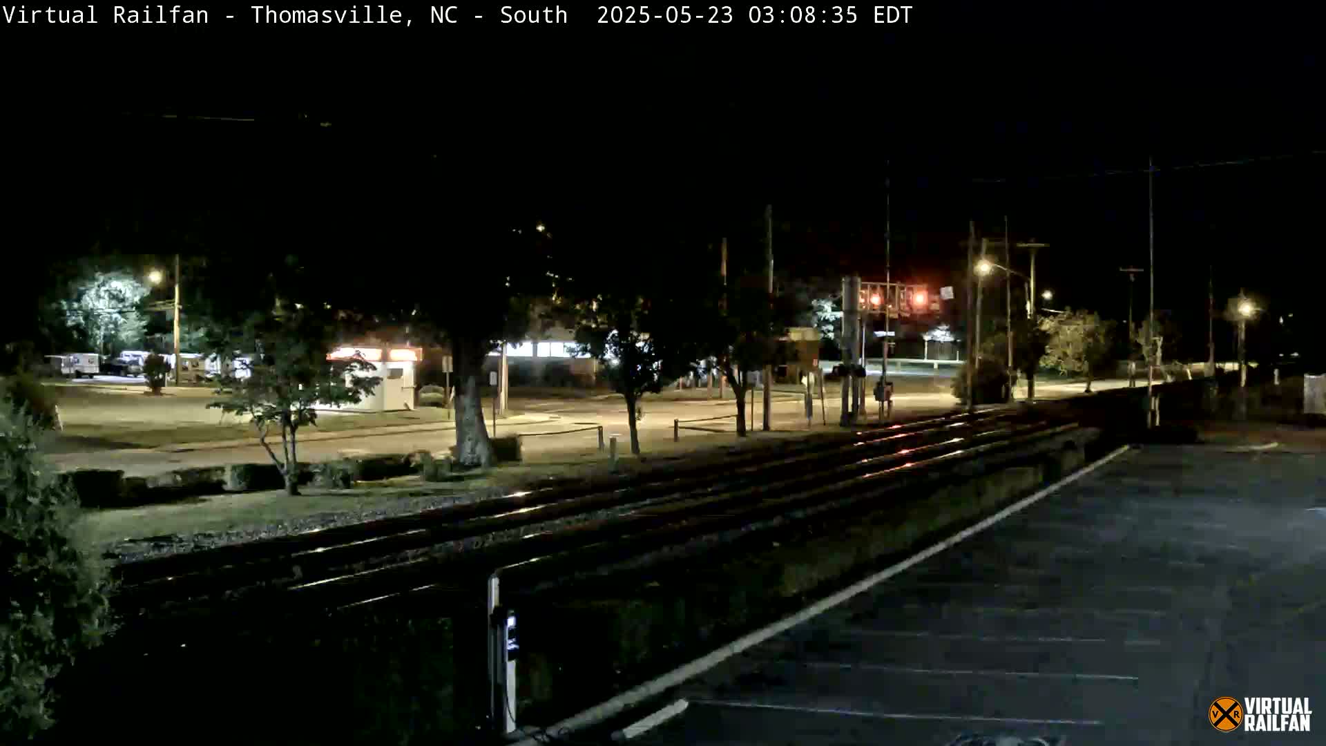 At night, a nighttime view shows railroad tracks next to a road with sparse traffic and some streetlights visible in the background.