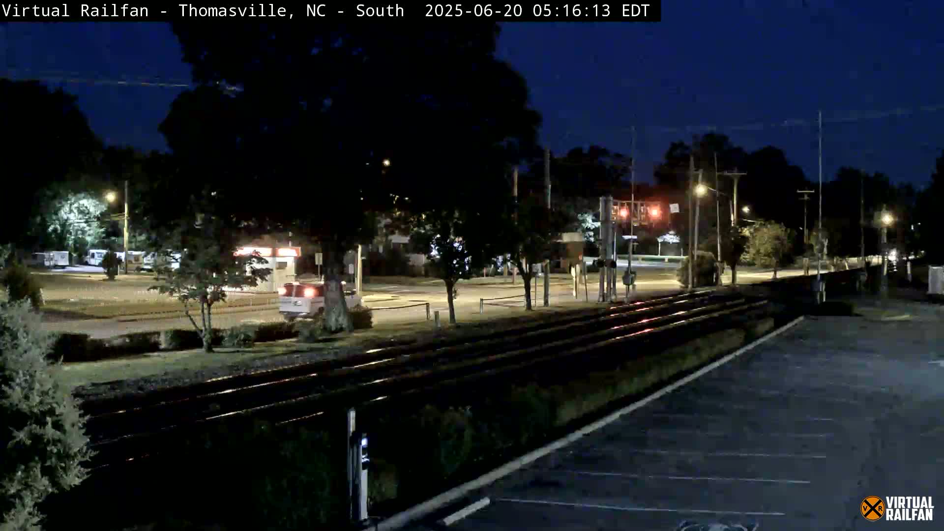 A nighttime view of railroad tracks beside a road with sparse traffic, under a clear dark sky.