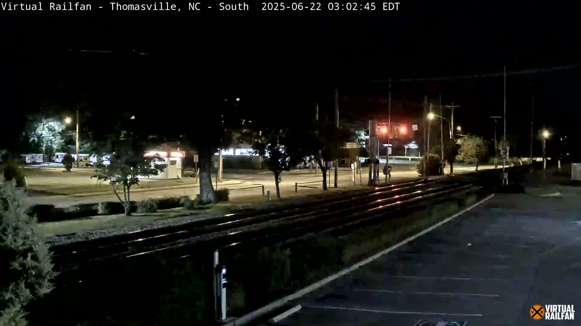 A nighttime view of railroad tracks adjacent to a road with sparse nighttime traffic, under a clear sky.