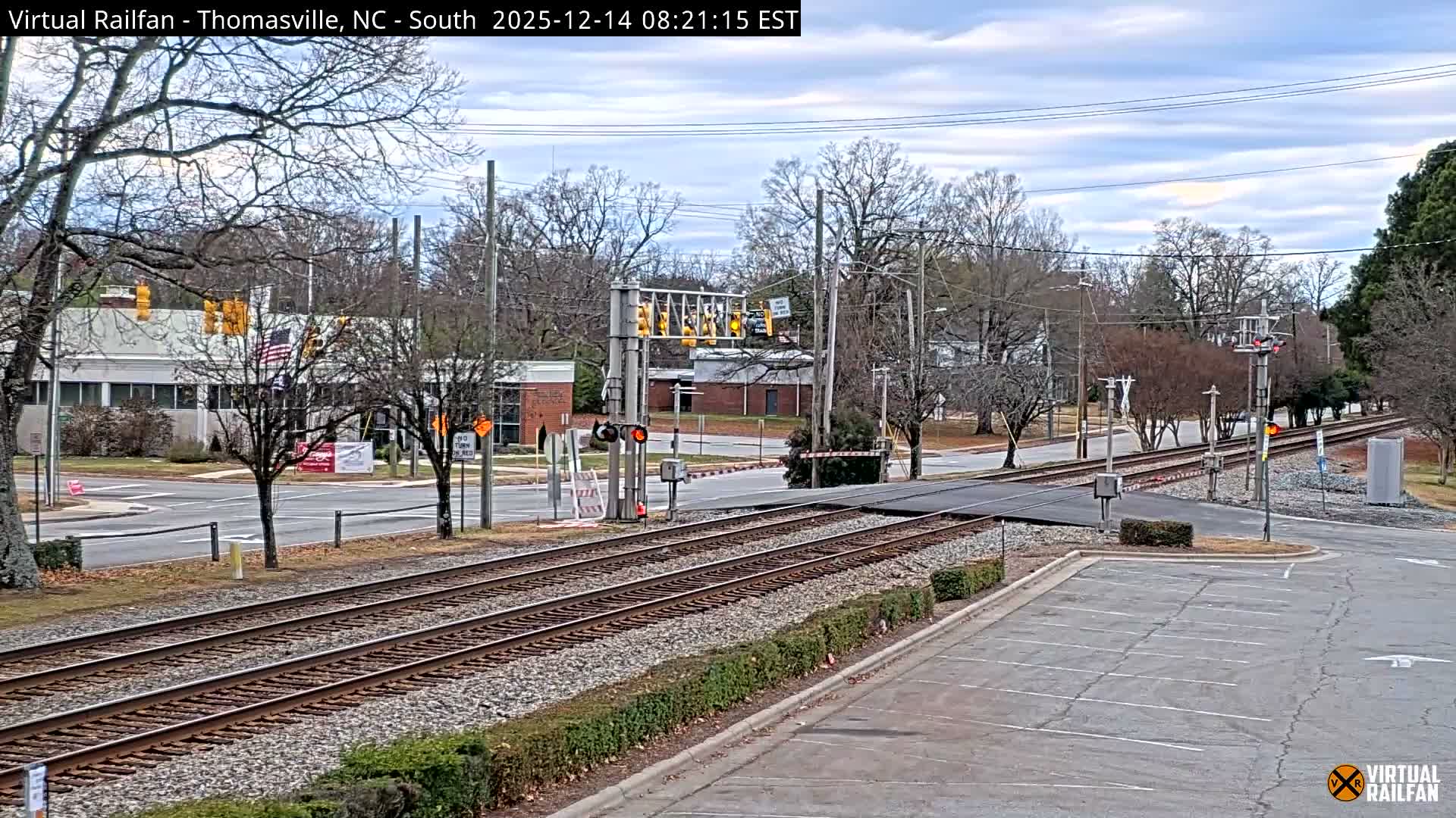 The image displays a white background featuring a prominent orange and black circular logo resembling a railroad crossing sign with "V" and "R" letters in the top center, and a smaller, faded version of the same logo in the bottom right corner.