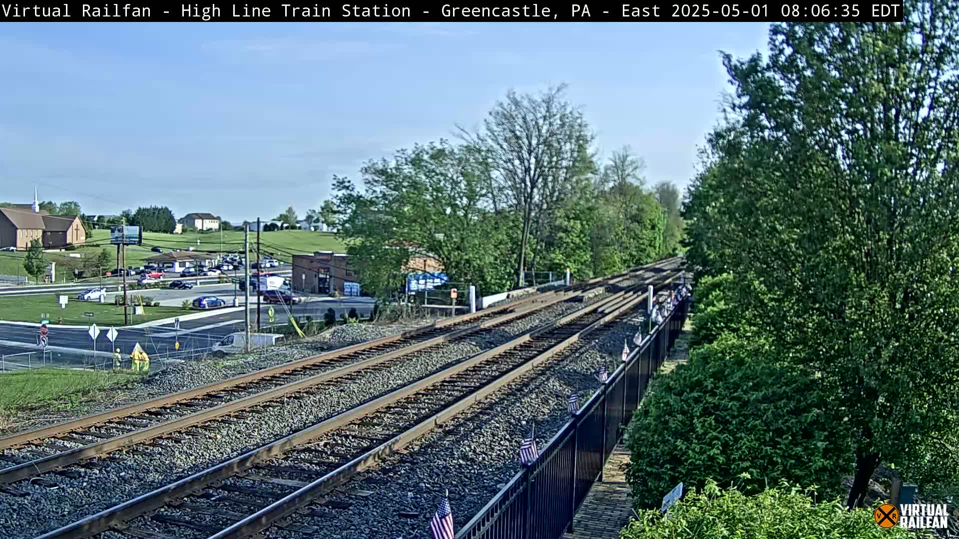 Multiple train tracks extend from a small town under a clear, sunny sky.