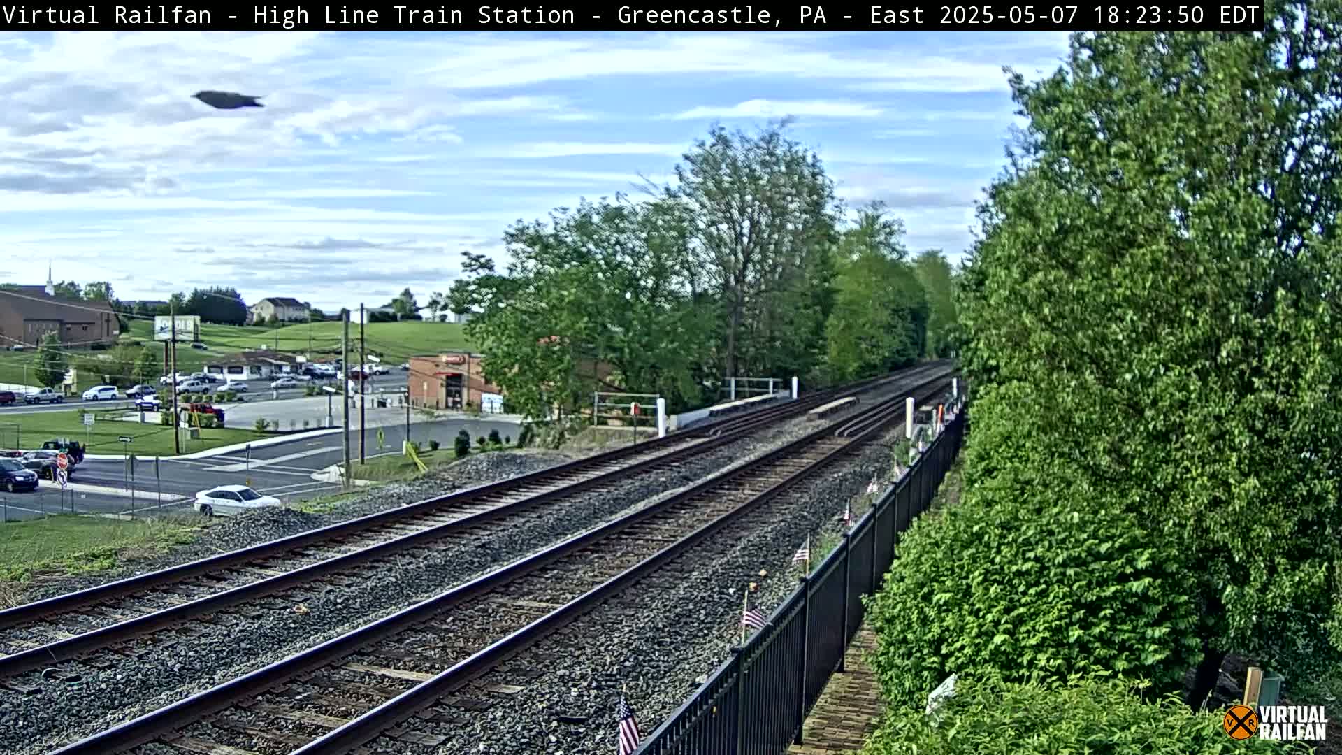 A high-angle view of train tracks extending into the distance, under a partly cloudy sky, with a small town visible in the background.