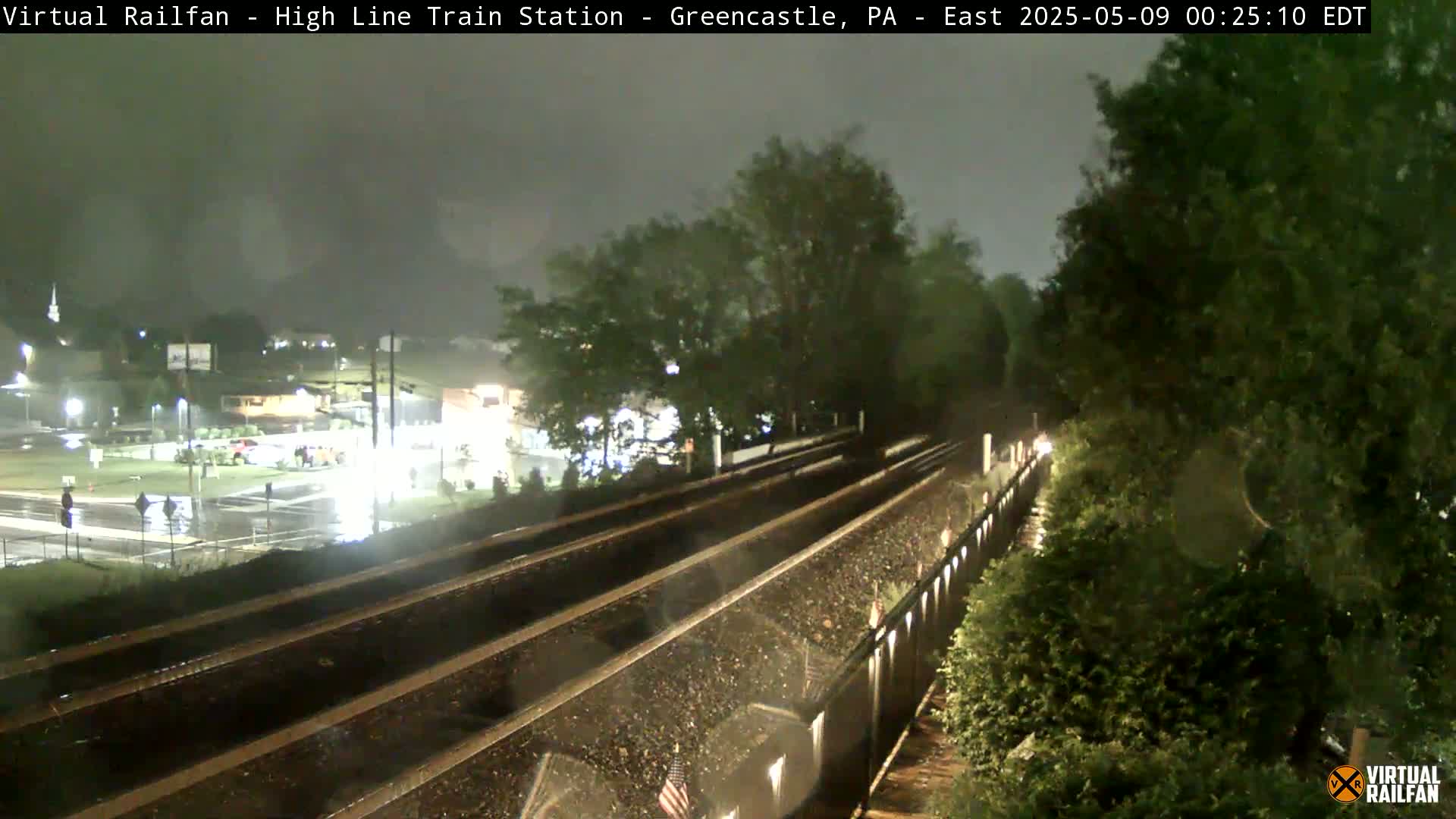 A nighttime view of rain-slicked train tracks and a nearby intersection under a dark, overcast sky.