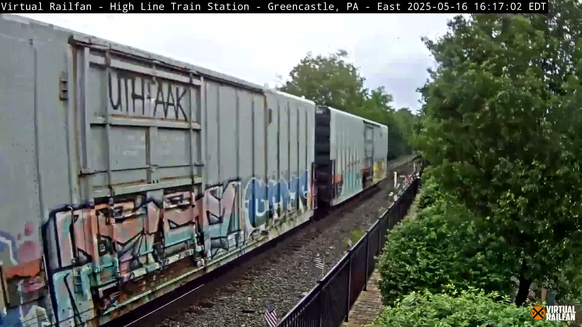 A freight train with graffiti-covered cars passes by on a partly cloudy day.