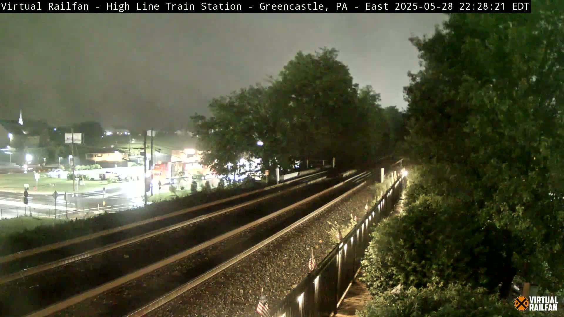 Three sets of train tracks under a dark, overcast sky, with wet pavement visible in the distance.