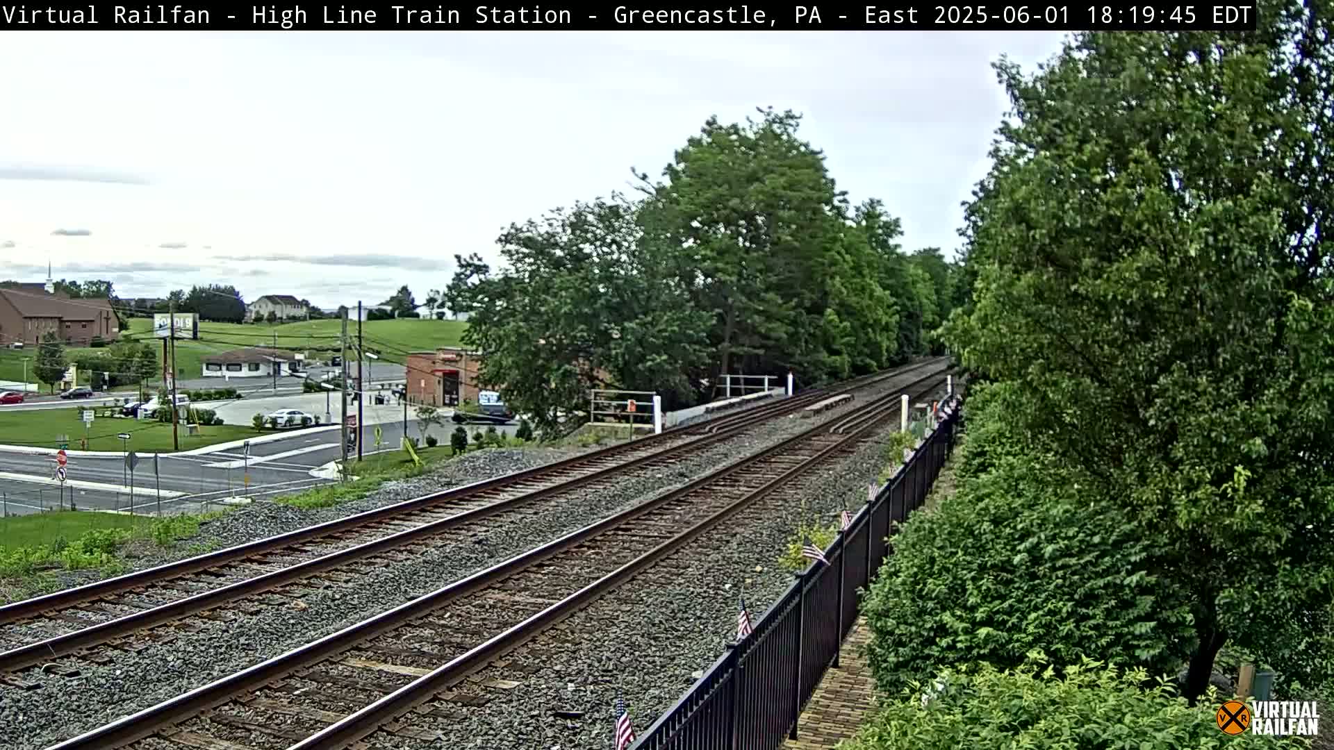 Train tracks extend into the distance, passing through a lush green landscape under a partly cloudy sky.