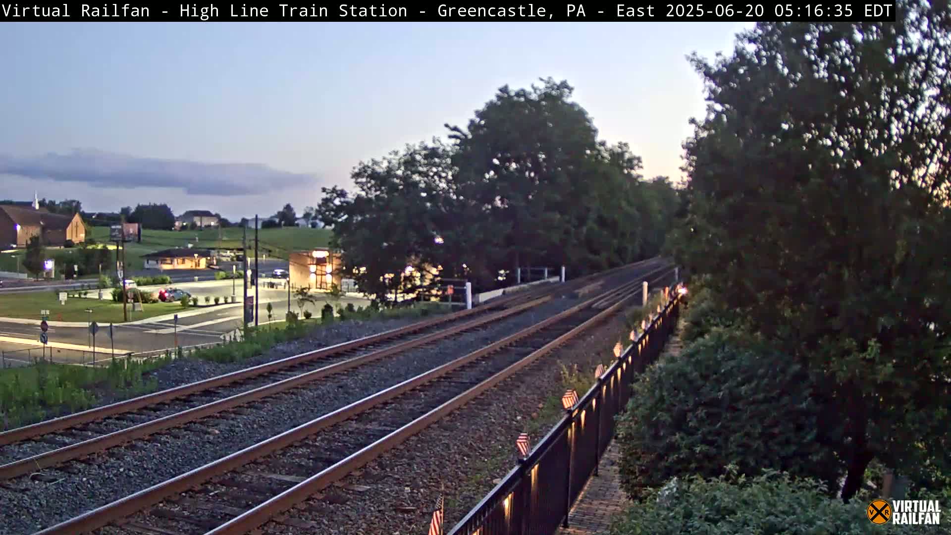 Train tracks extend from a small town into a landscape of trees under a twilight sky.