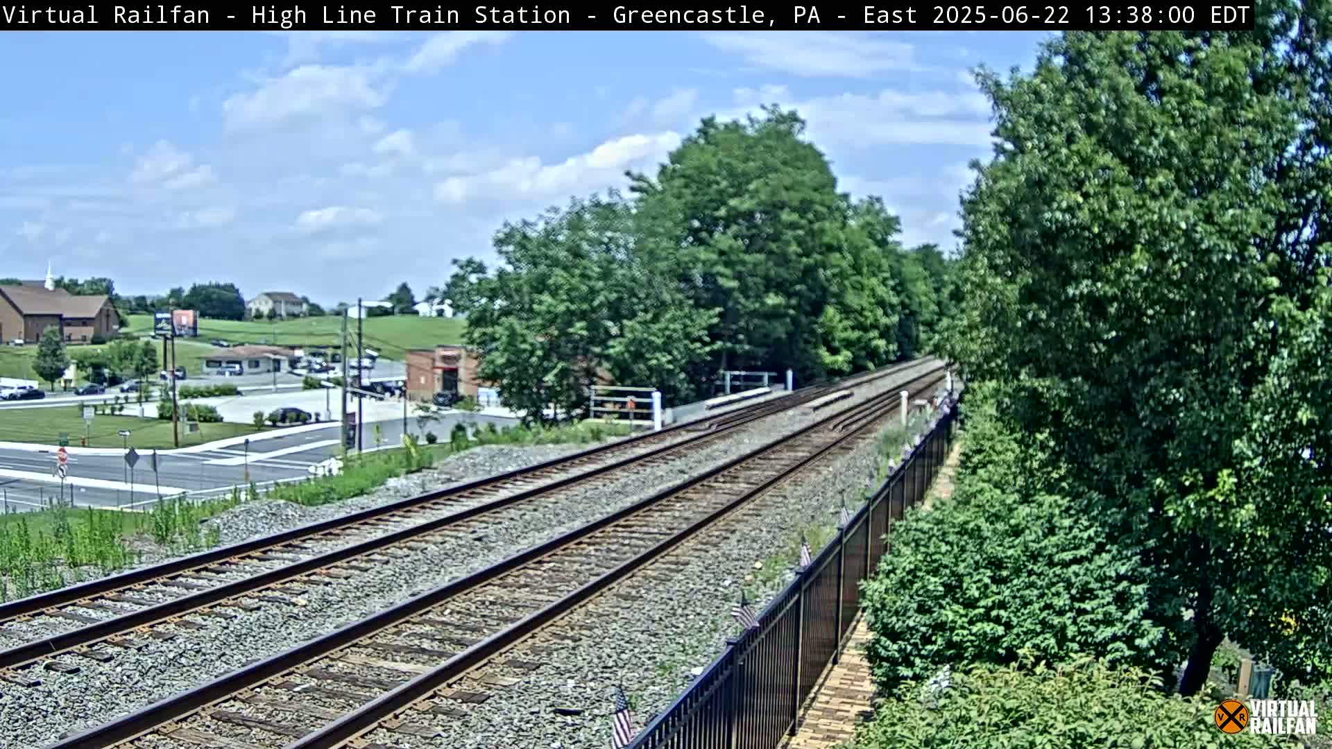 A view of a train track leading to a small town under a partly cloudy sky.