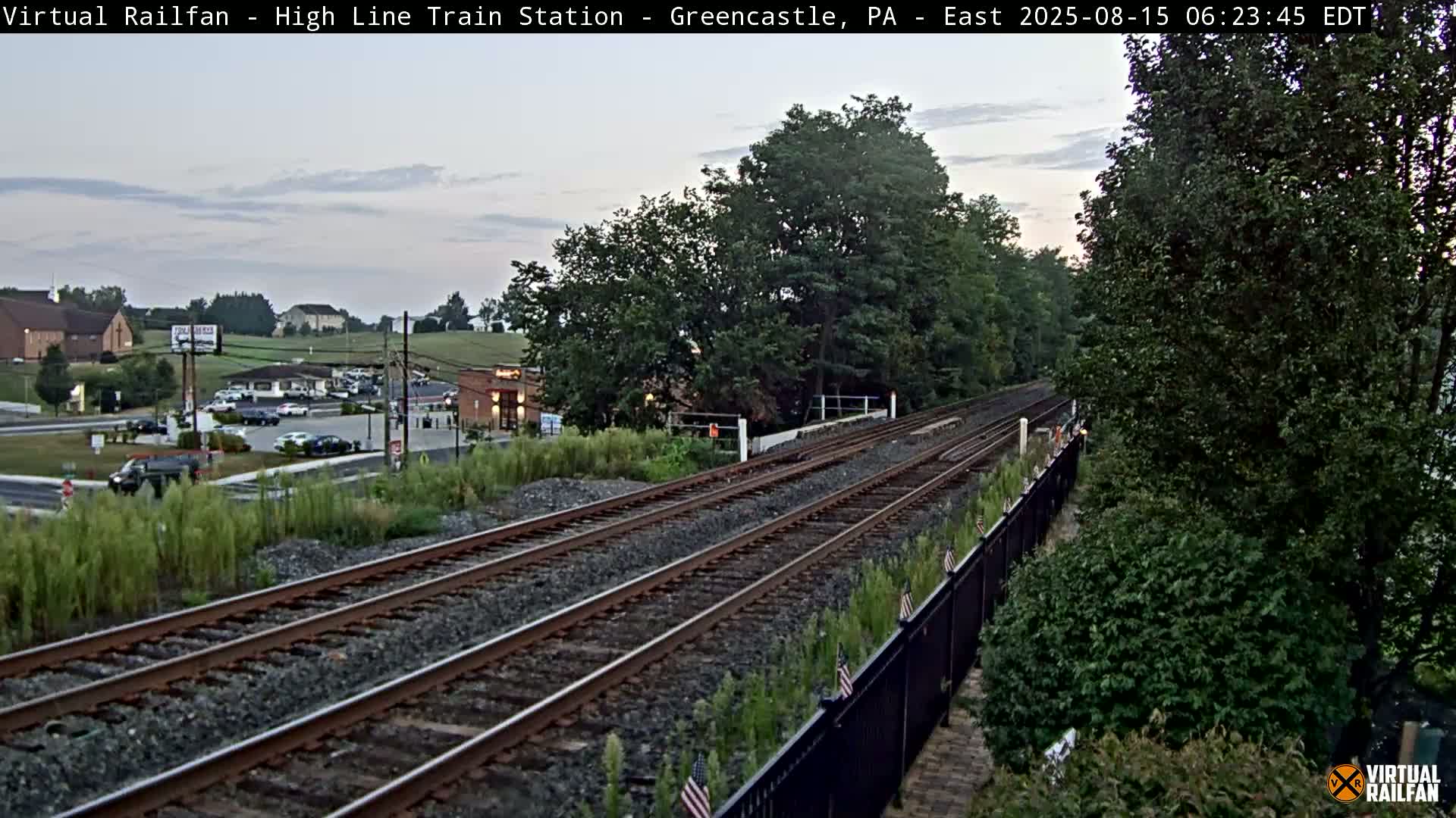 A nighttime view of a train of covered hopper cars moving along railroad tracks beside a tree-lined embankment.
