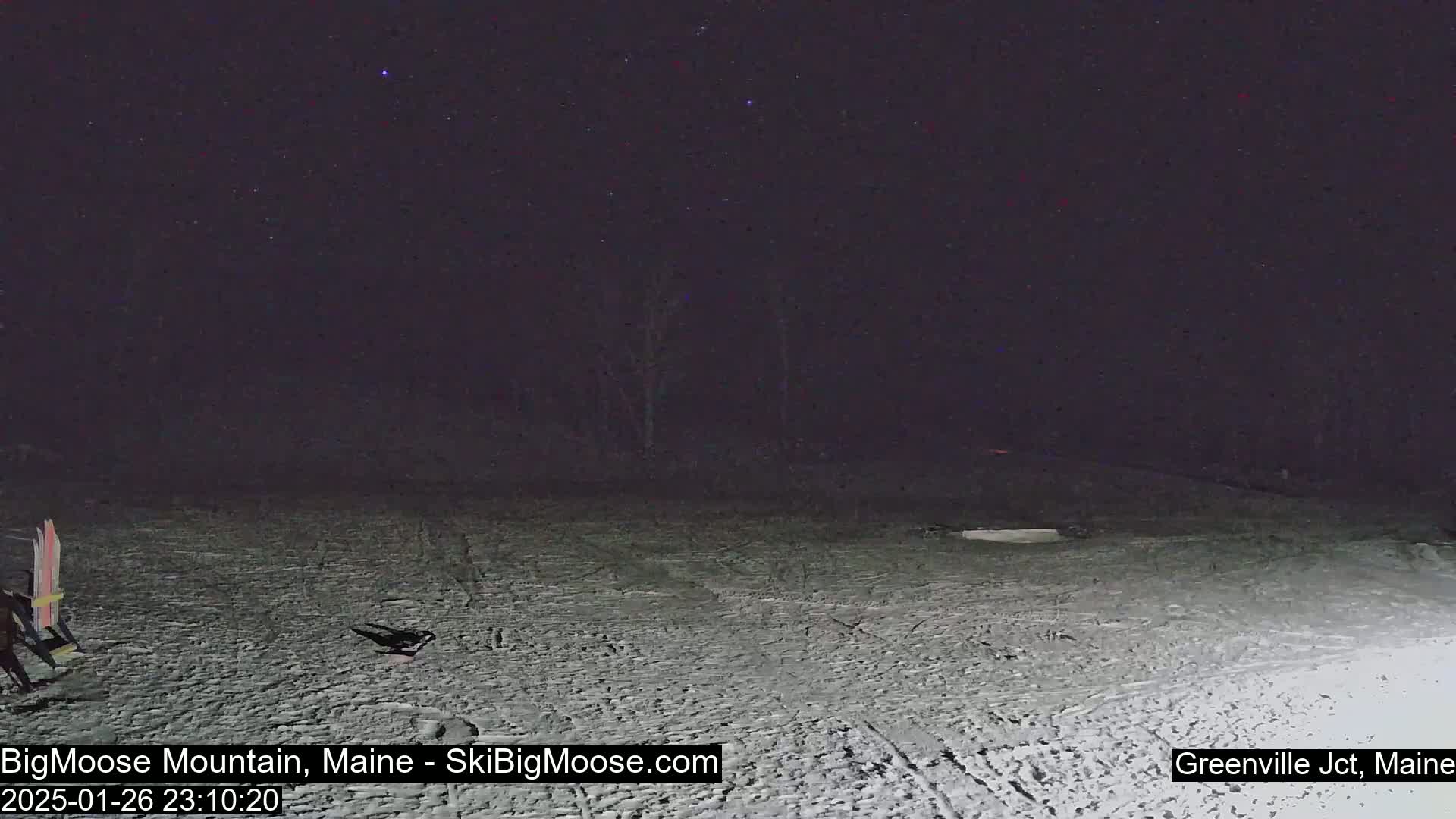 Under a clear, starry night sky, a snow-covered area shows faint tracks in the snow and some objects near the bottom left.