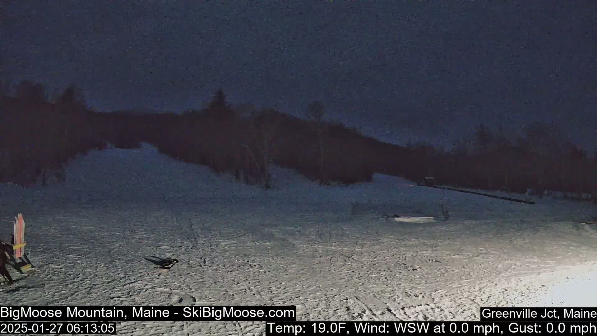 Under a dark night sky, a snow-covered slope is visible, with some minimal activity near the bottom.