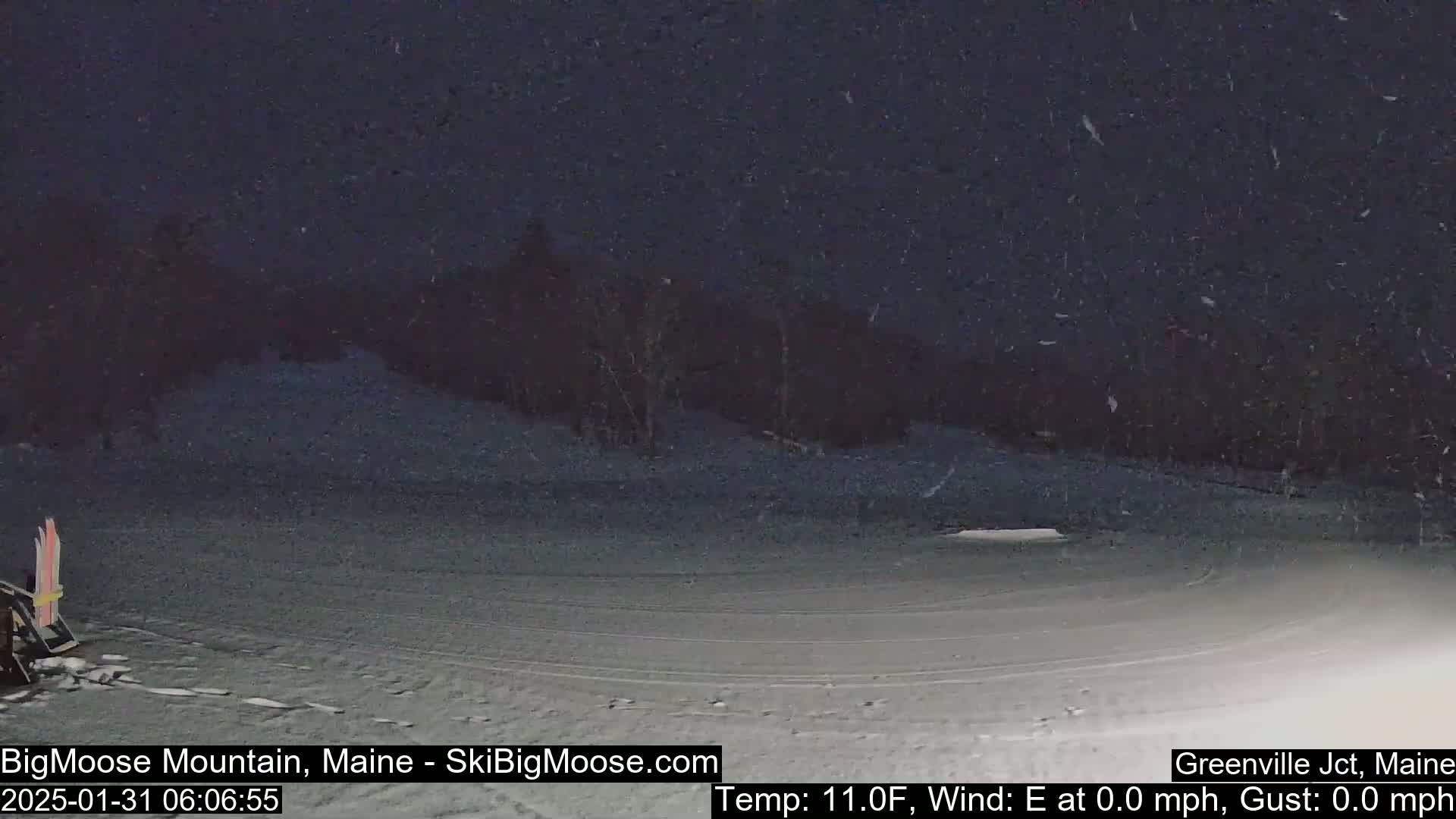 A snow-covered ski slope is visible at night under light snowfall.