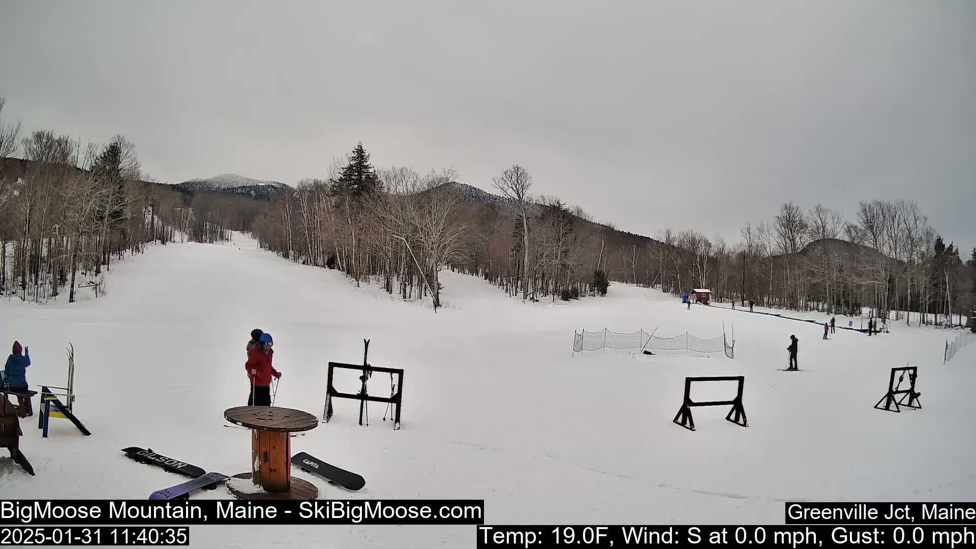 A snow-covered ski slope with sparsely populated skiers and snowboarders, under an overcast sky.
