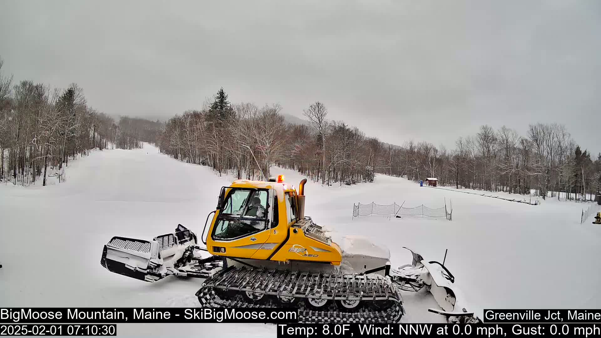 A yellow snow groomer sits on a snow-covered ski slope under an overcast sky.