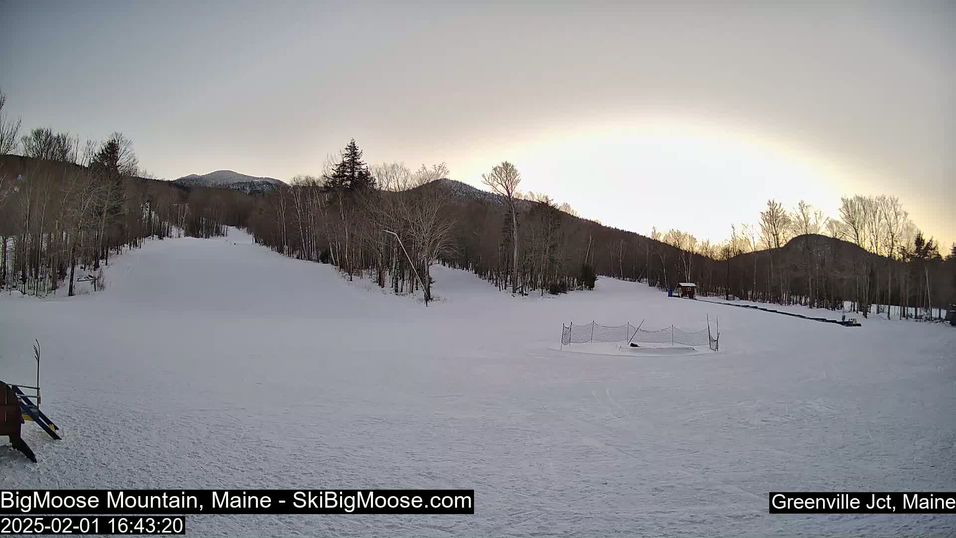 A snow-covered ski slope with trees and mountains in the background under a twilight sky.
