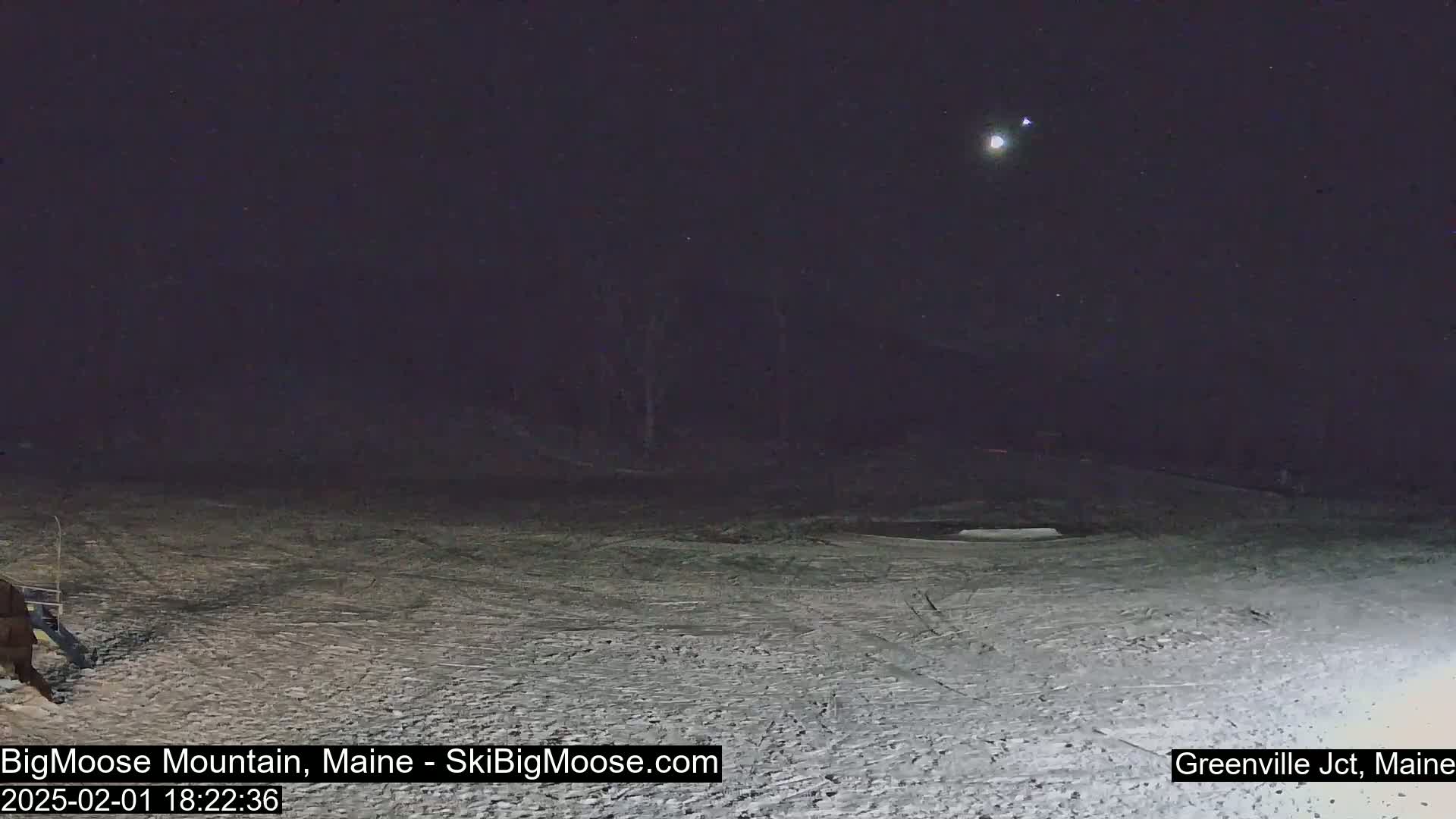 A snow-covered ski slope is visible under a dark night sky with a bright moon and stars.