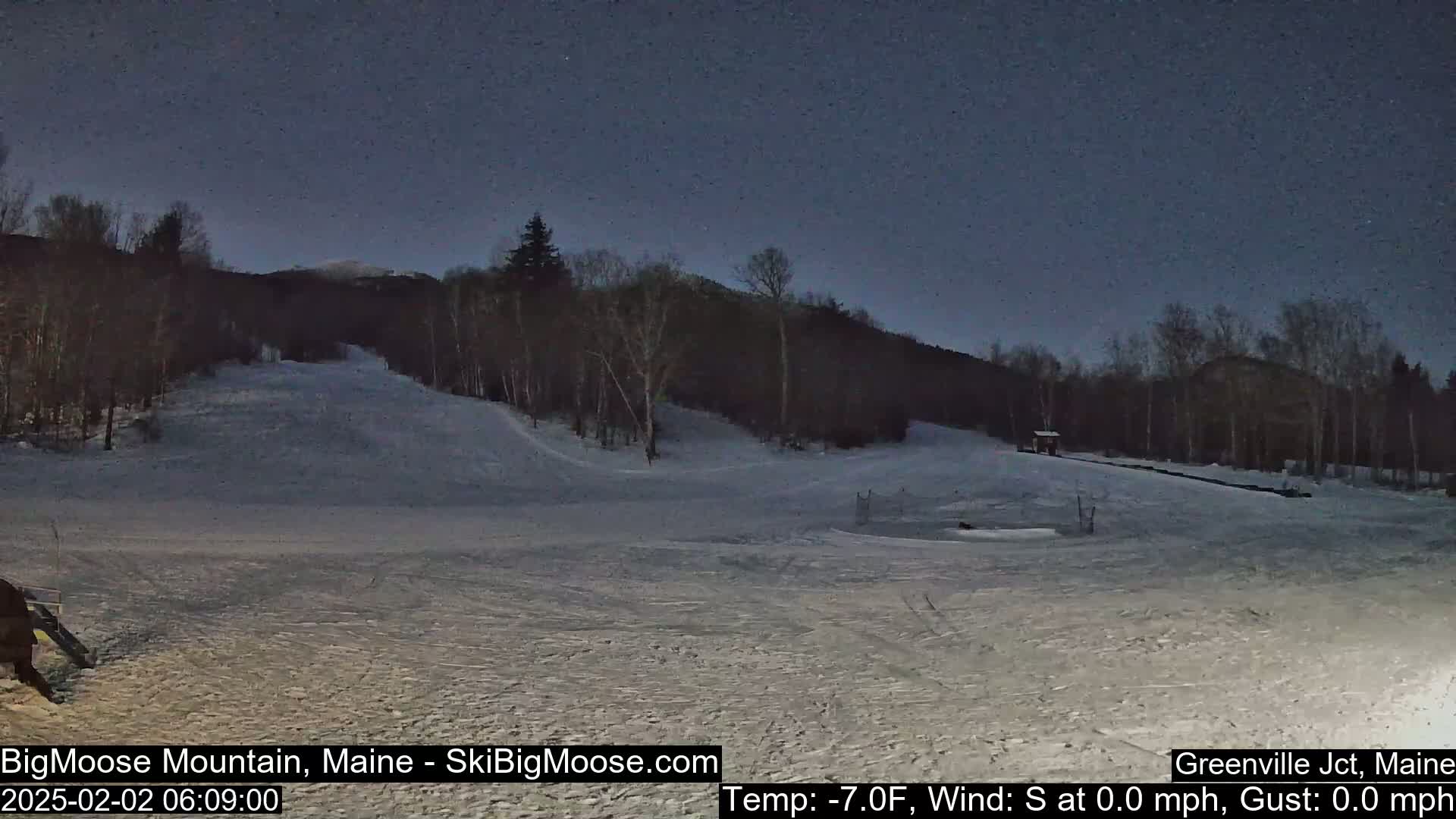 A snow-covered ski slope is visible under a dark night sky, with trees lining the background.